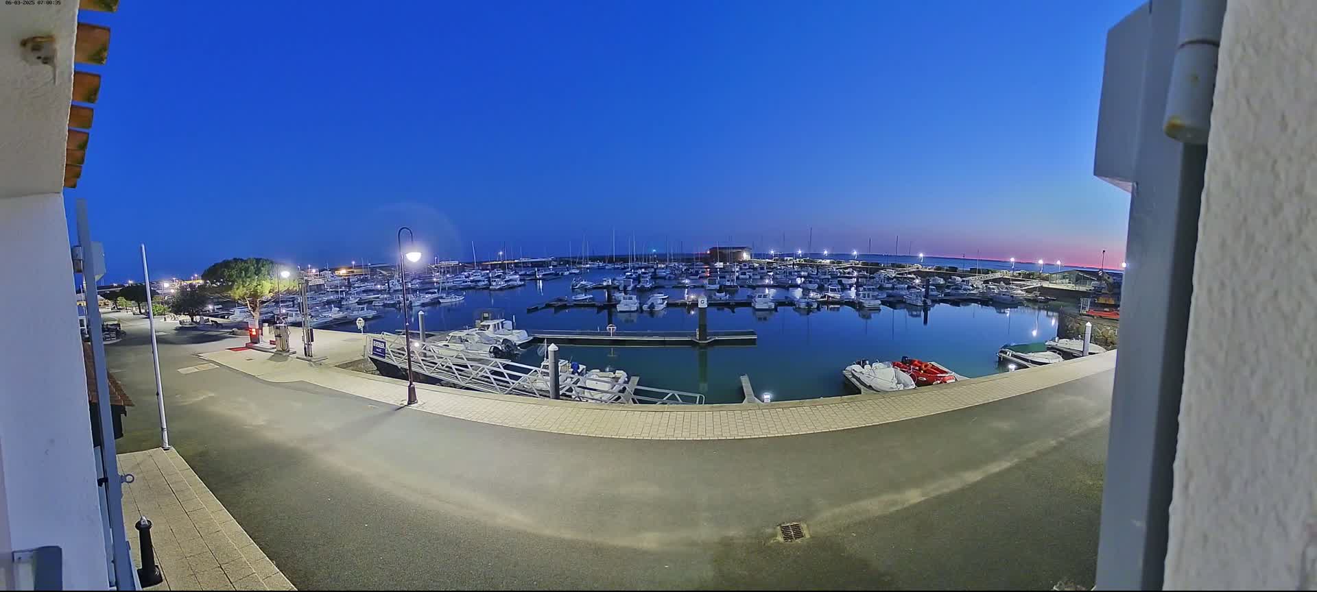 A marina filled with numerous boats is visible at twilight under a clear, dark blue sky.