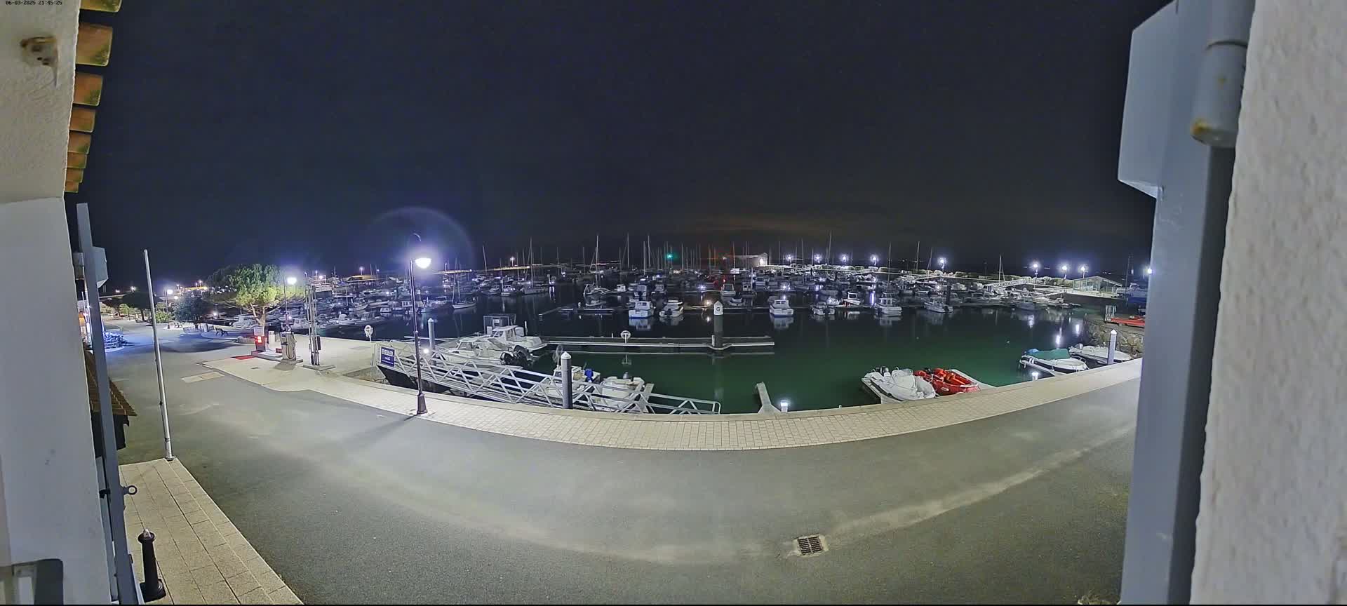 A nighttime view of a marina filled with boats, illuminated by streetlights, under a dark sky.