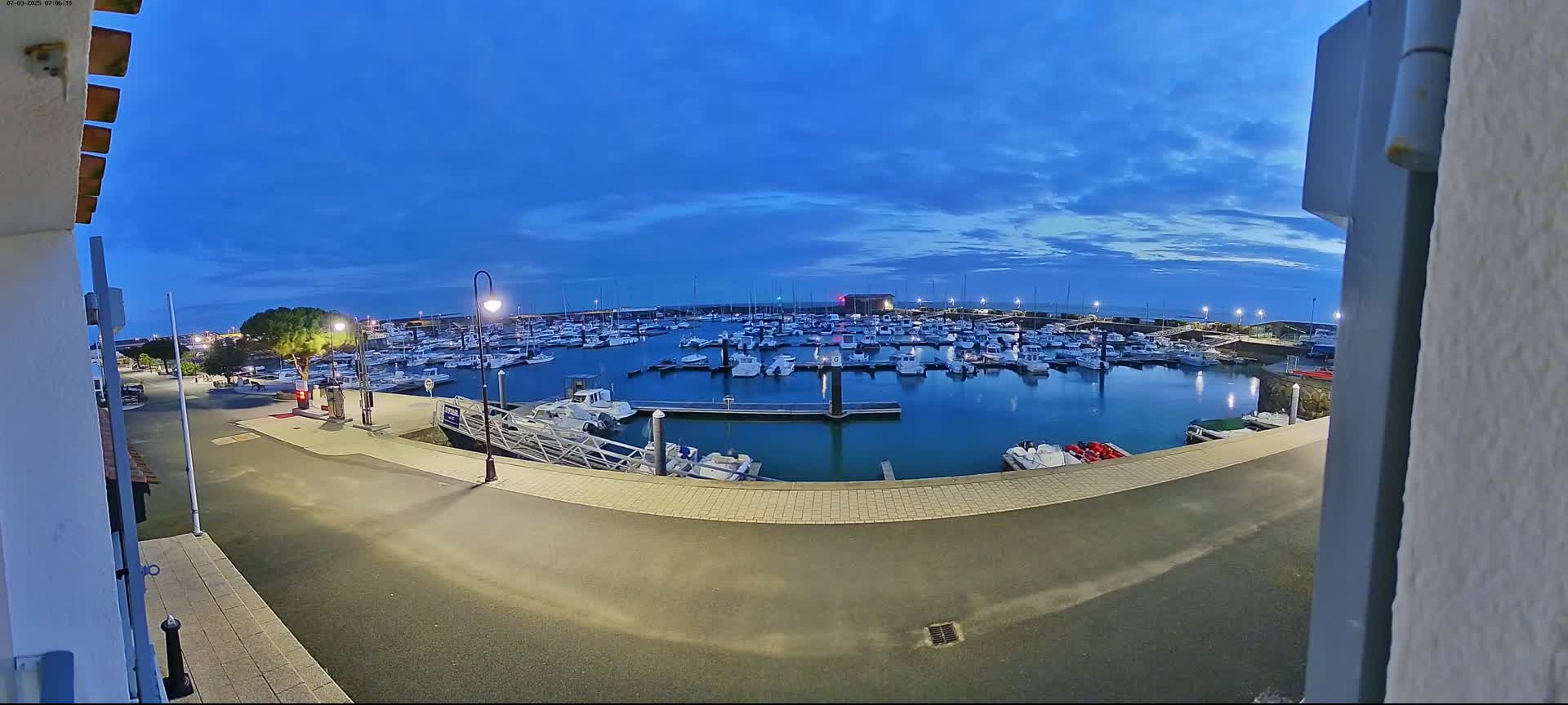 A marina filled with many boats is seen at dusk under a mostly clear blue sky.