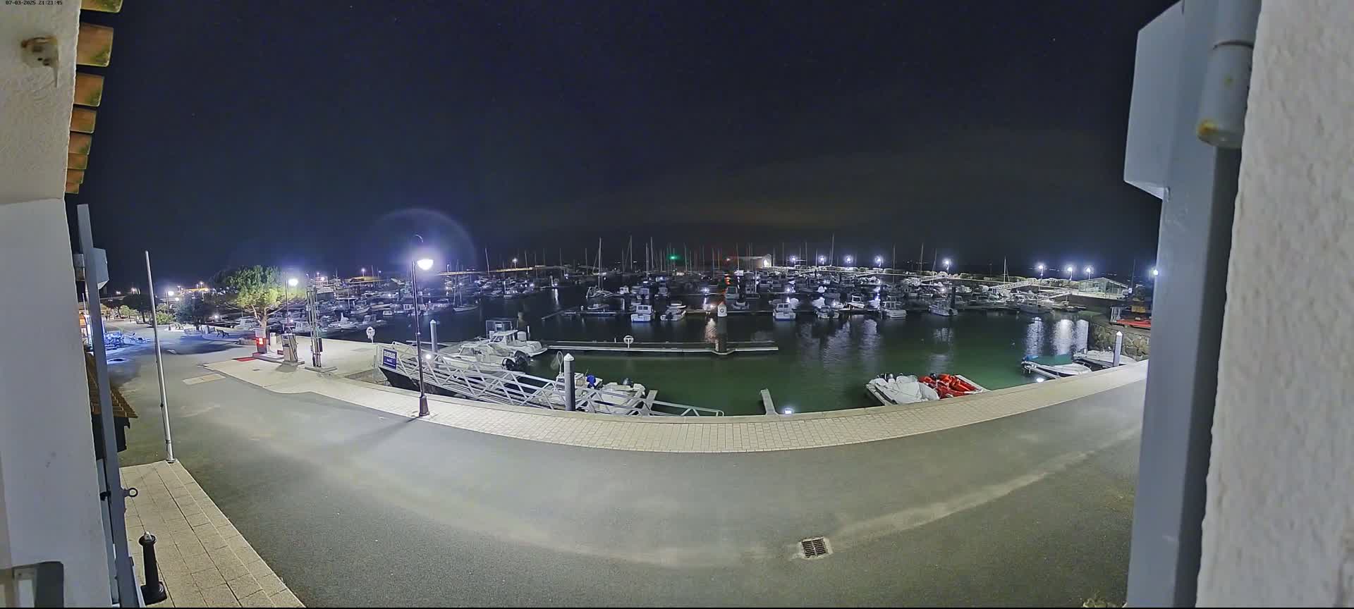 A nighttime view of a marina filled with docked boats, illuminated by streetlights under a clear, starry sky.