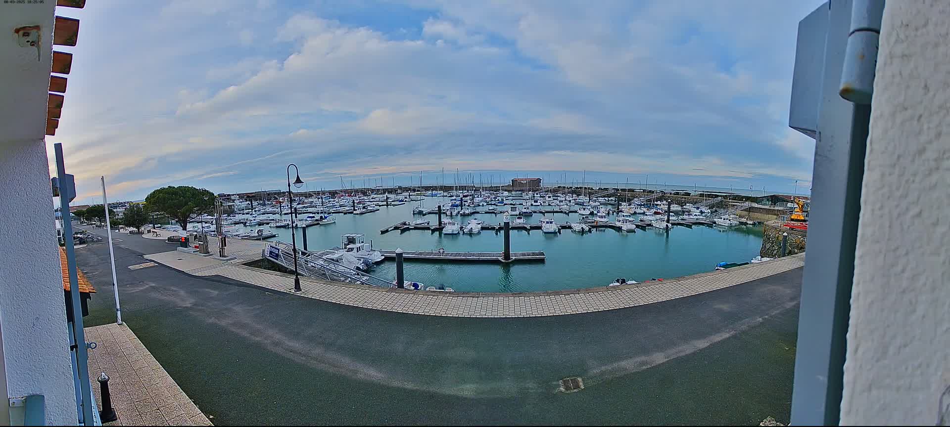 A marina filled with numerous boats is seen under a partly cloudy sky.