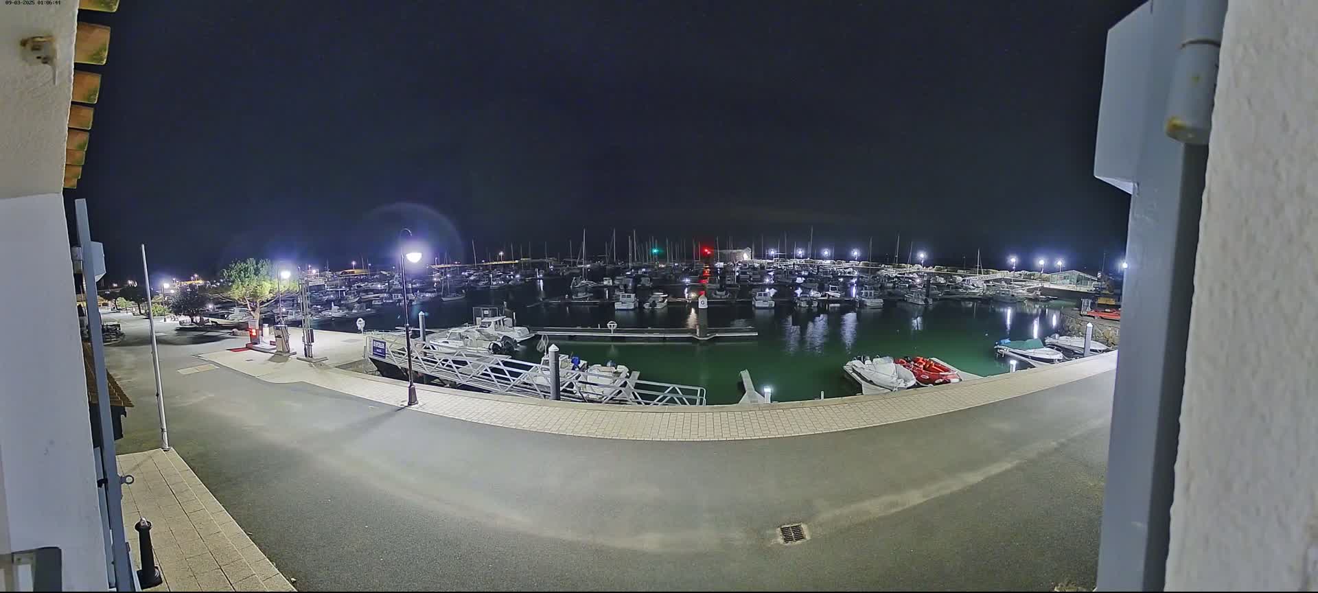 A nighttime view of a marina filled with numerous boats, illuminated by artificial lights under a clear, dark sky.