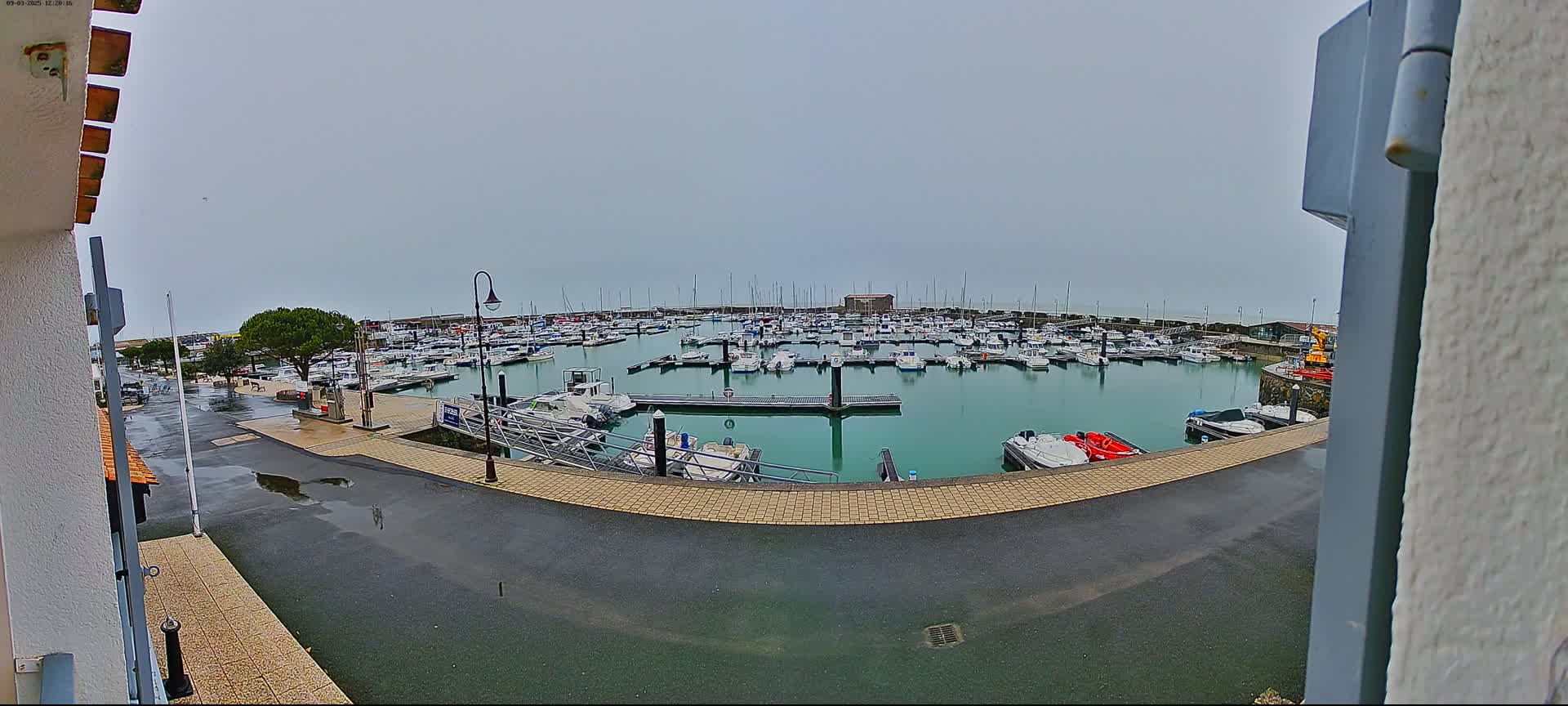 A wet marina filled with numerous boats is viewed from a slightly elevated position on an overcast day.