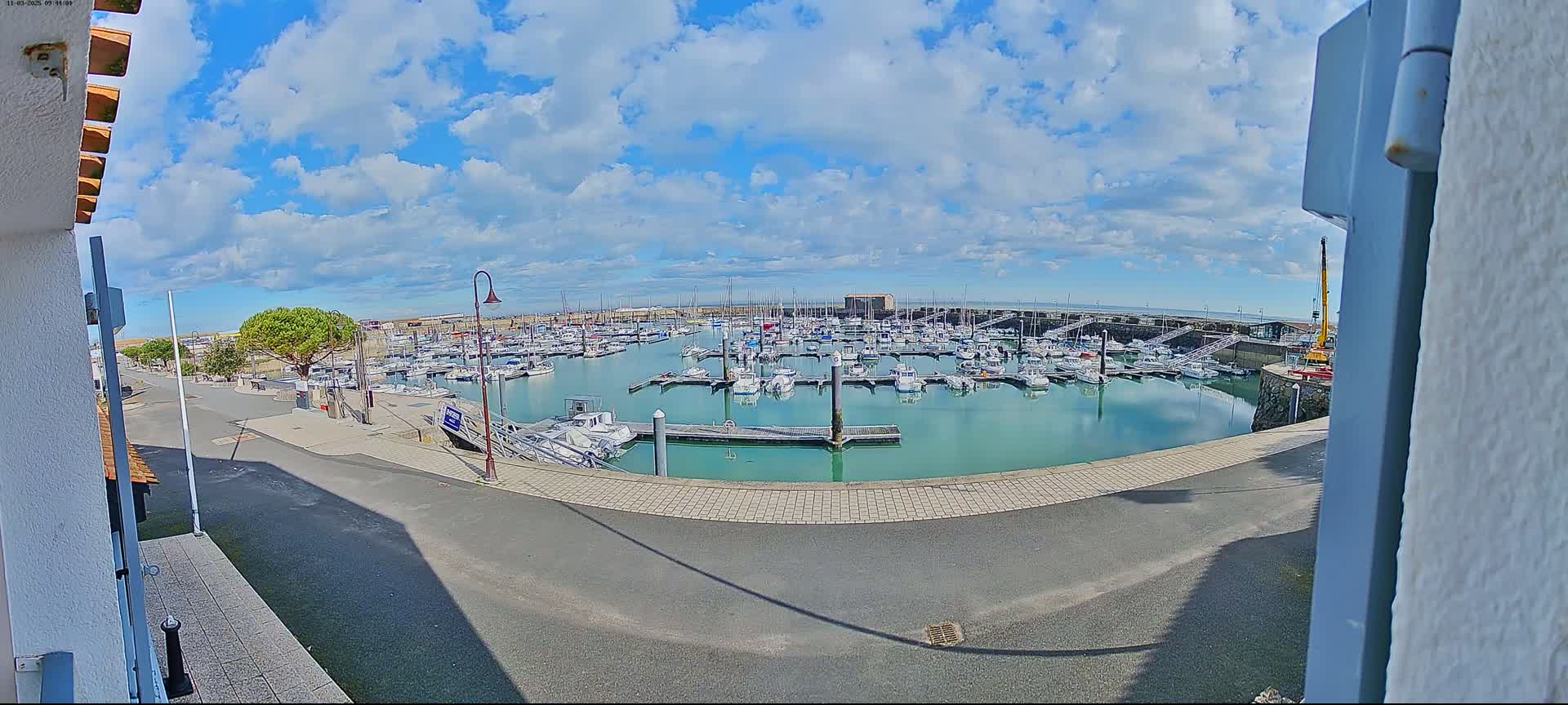 A marina filled with numerous boats is visible under a partly cloudy sky.