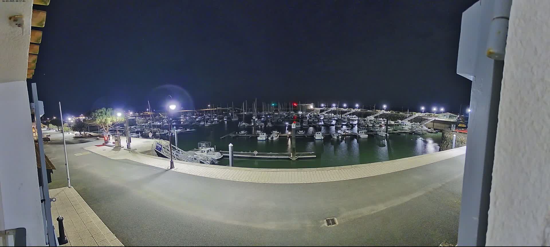 A nighttime view of a marina filled with numerous boats, illuminated by artificial lights under a clear, dark sky.