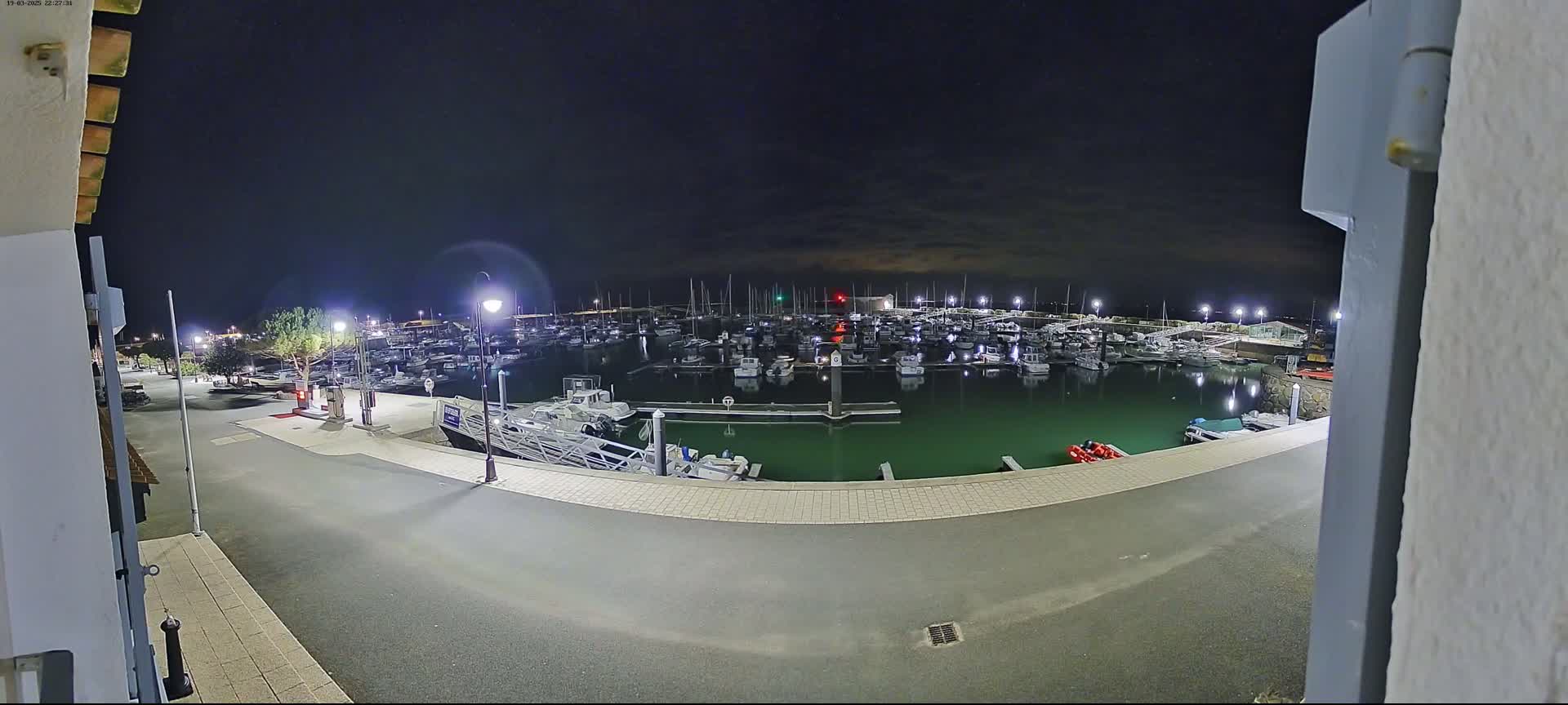 A nighttime view of a marina filled with boats, illuminated by streetlights under a dark, mostly clear sky.