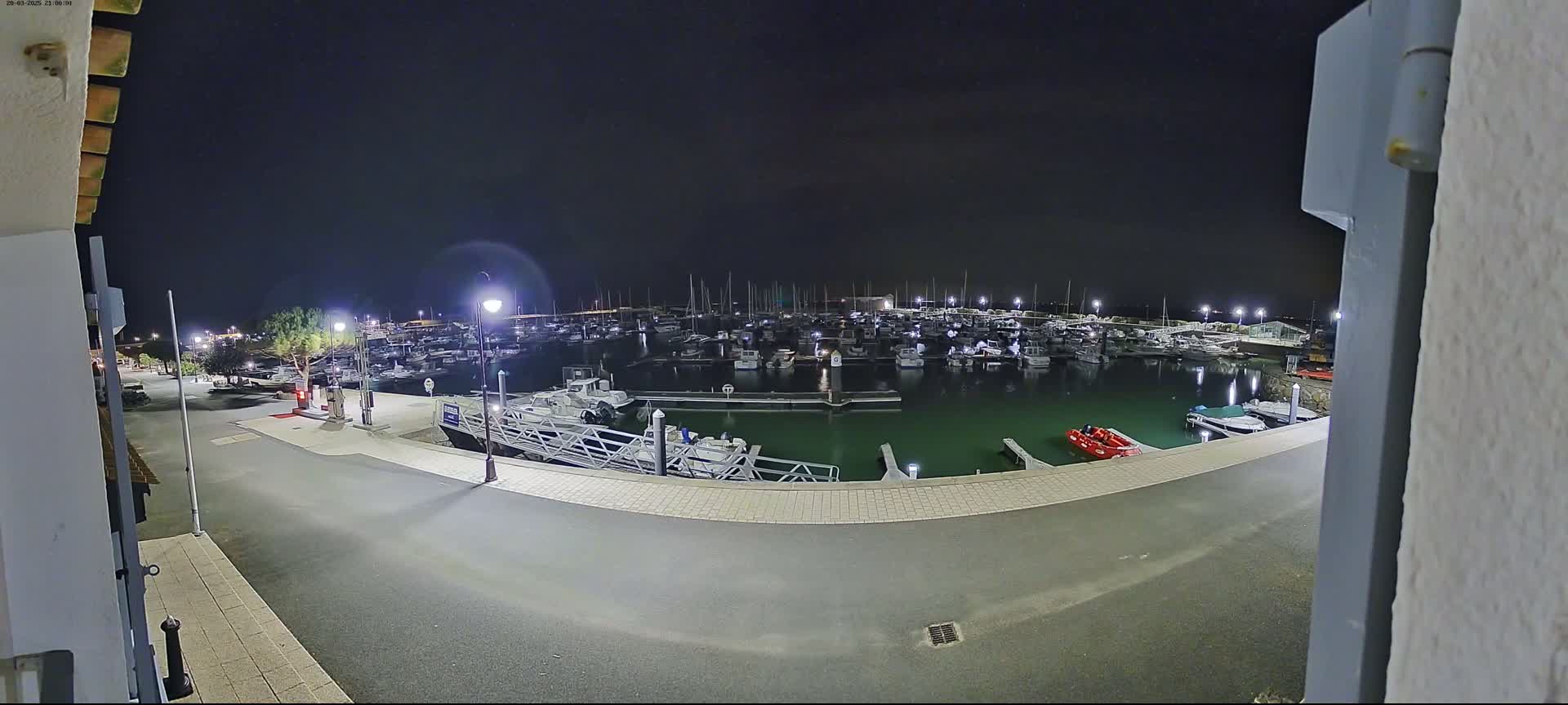 A nighttime view of a marina filled with numerous boats, illuminated by artificial lights, under a dark sky.