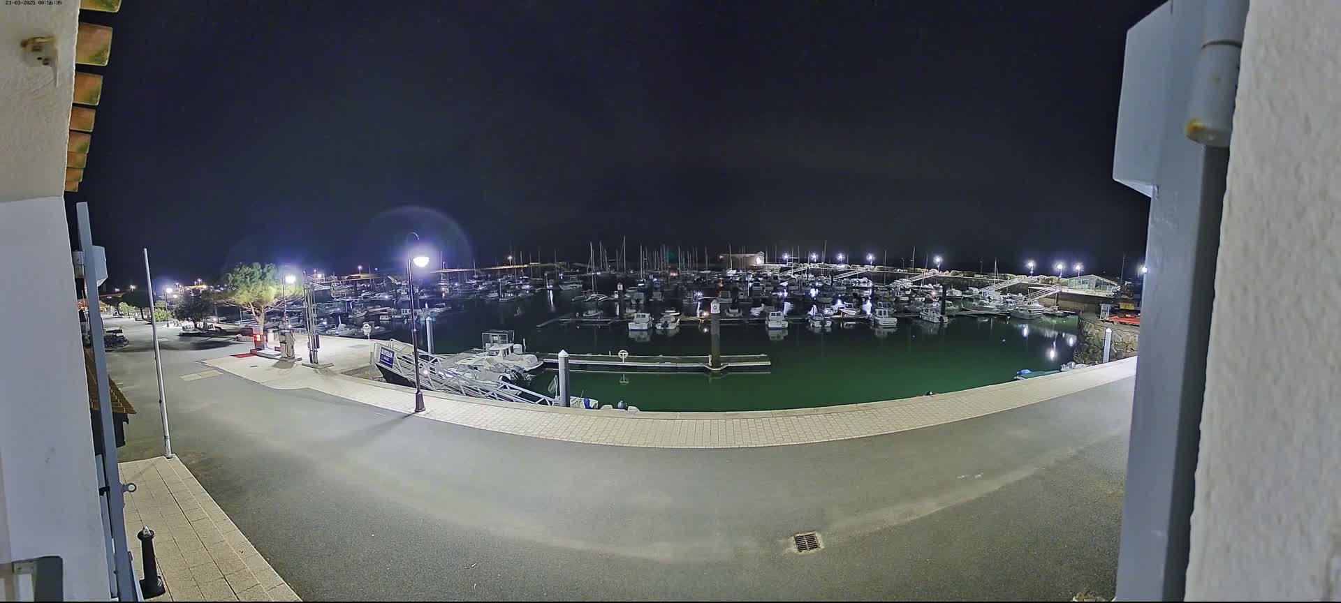 A nighttime view of a marina filled with numerous boats, illuminated by artificial lights under a dark sky.