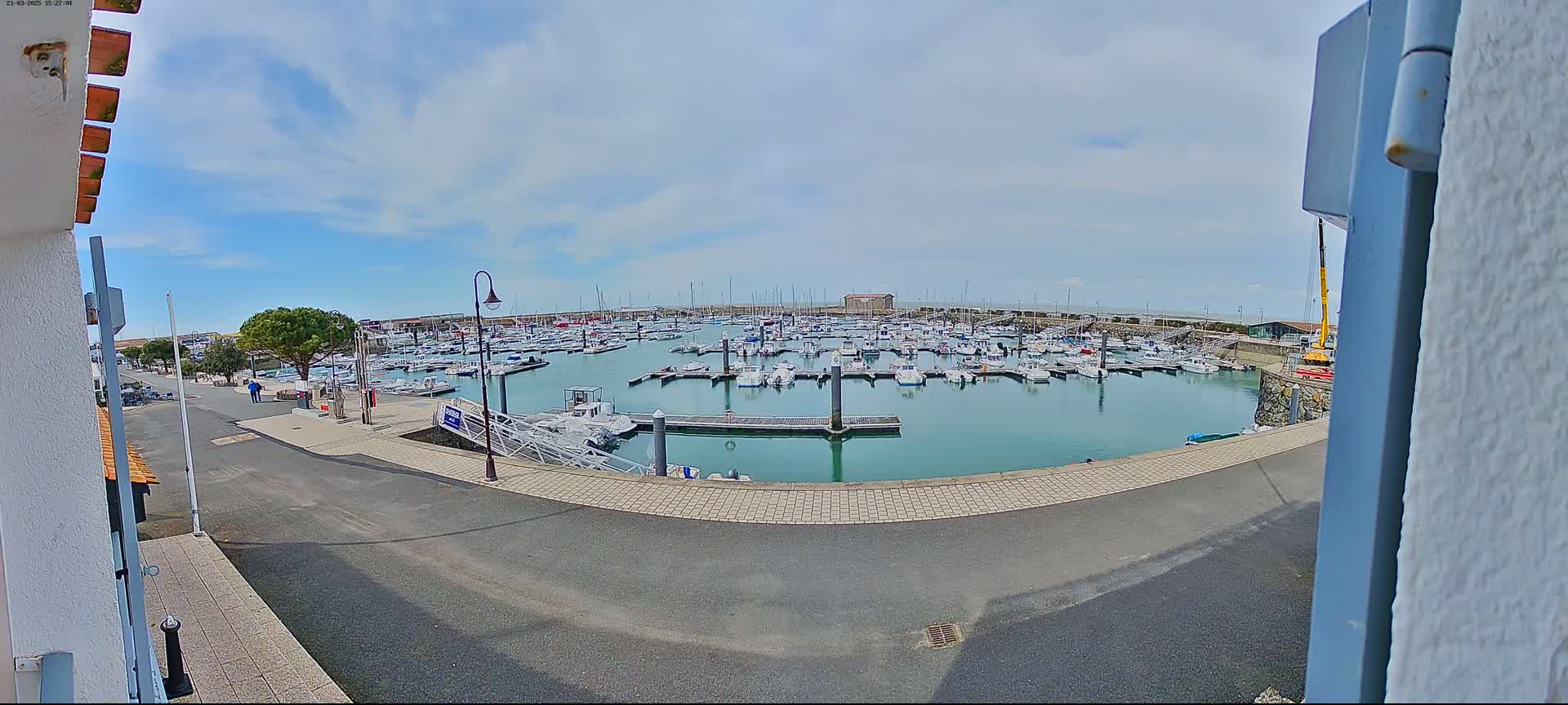 A marina filled with numerous boats under a partly cloudy sky is viewed from a slightly elevated vantage point.
