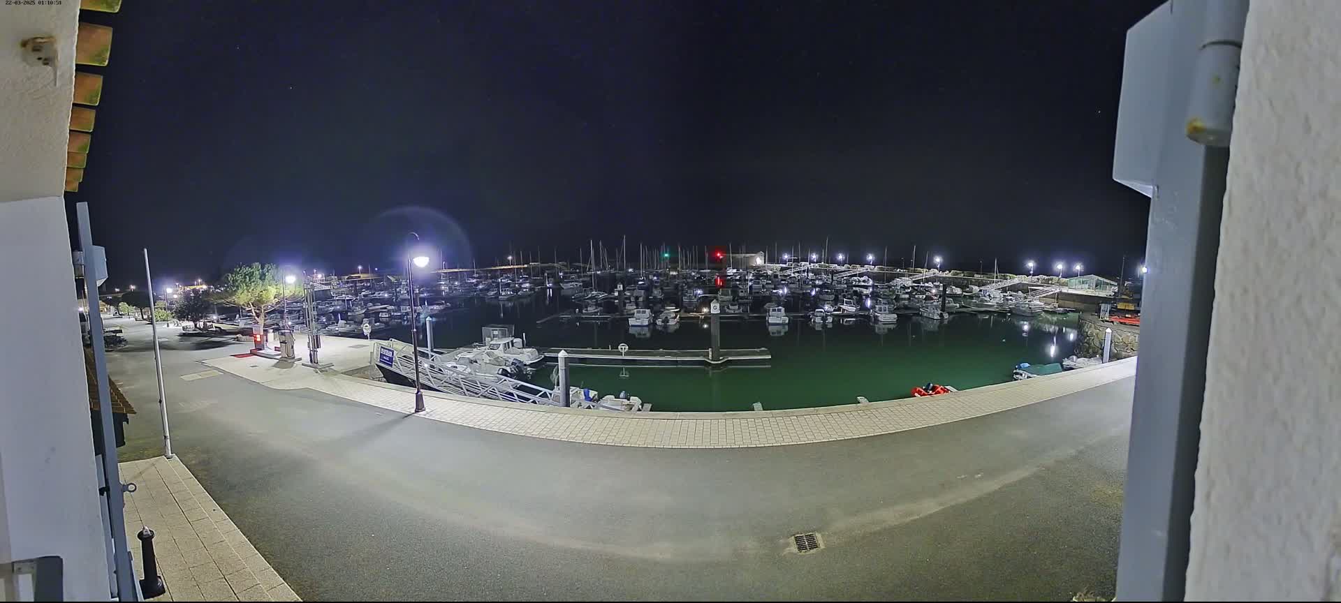 A nighttime view of a marina filled with numerous boats, illuminated by bright lights under a clear, dark sky.