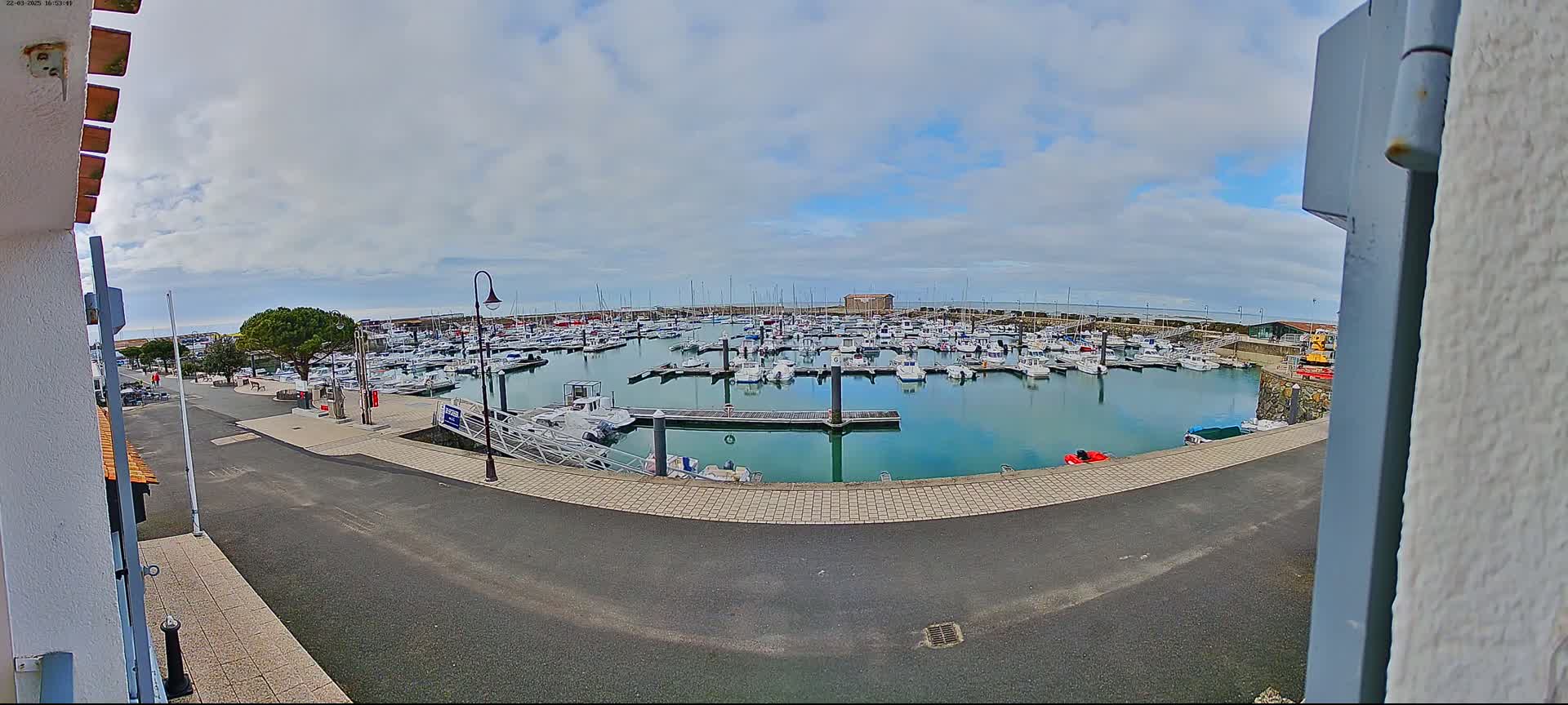 A marina filled with numerous boats is visible under a partly cloudy sky.