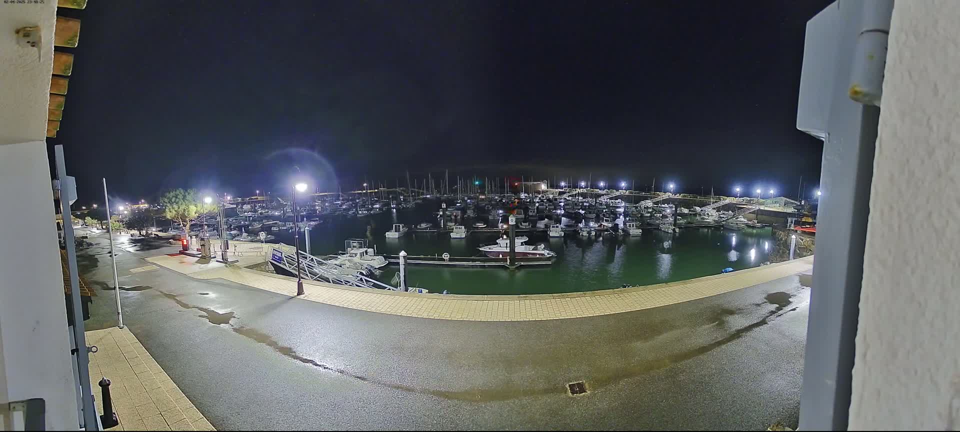 A wet, nighttime view of a marina filled with numerous boats, illuminated by artificial lights.
