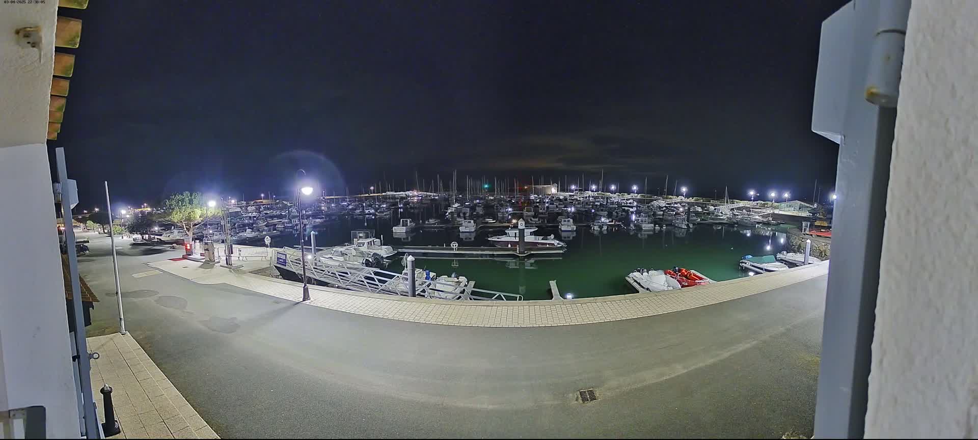A nighttime view of a marina filled with numerous boats, illuminated by artificial lights under a dark sky.