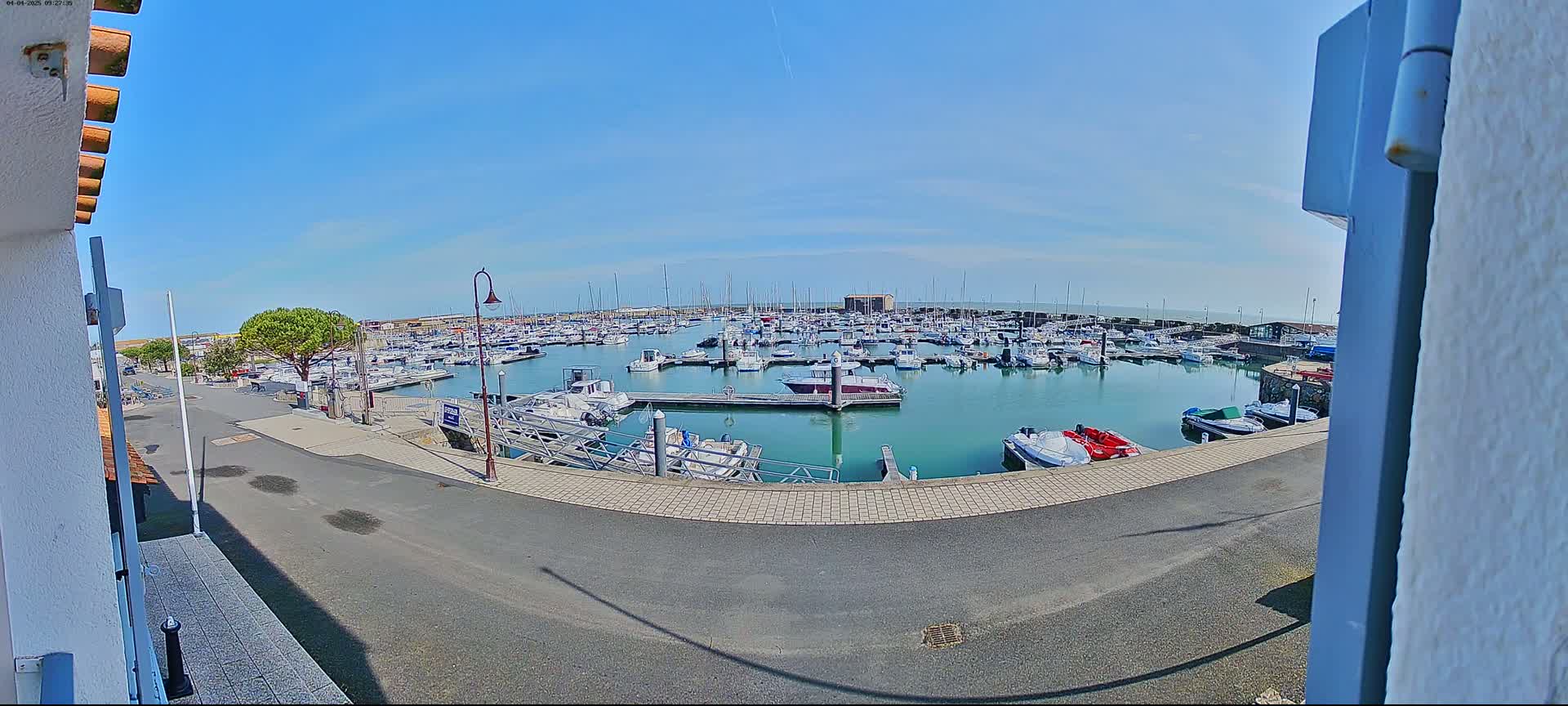 A marina filled with numerous boats is seen on a sunny day from a slightly elevated vantage point.