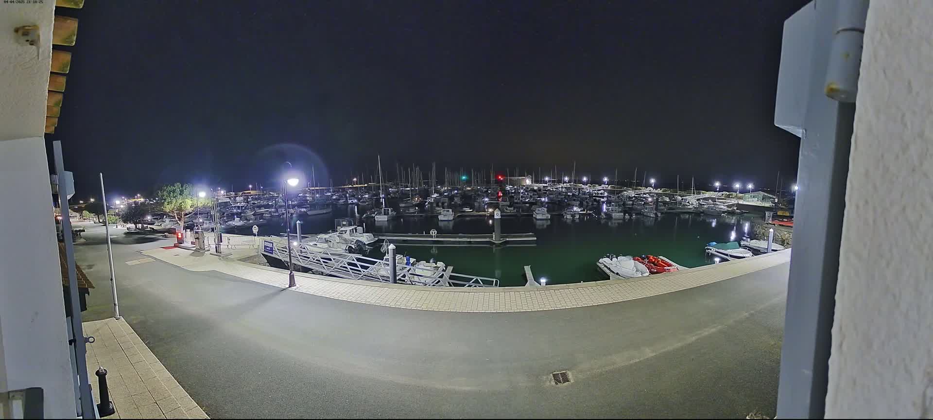 A nighttime view of a marina filled with boats, illuminated by several lights, under a clear, dark sky.