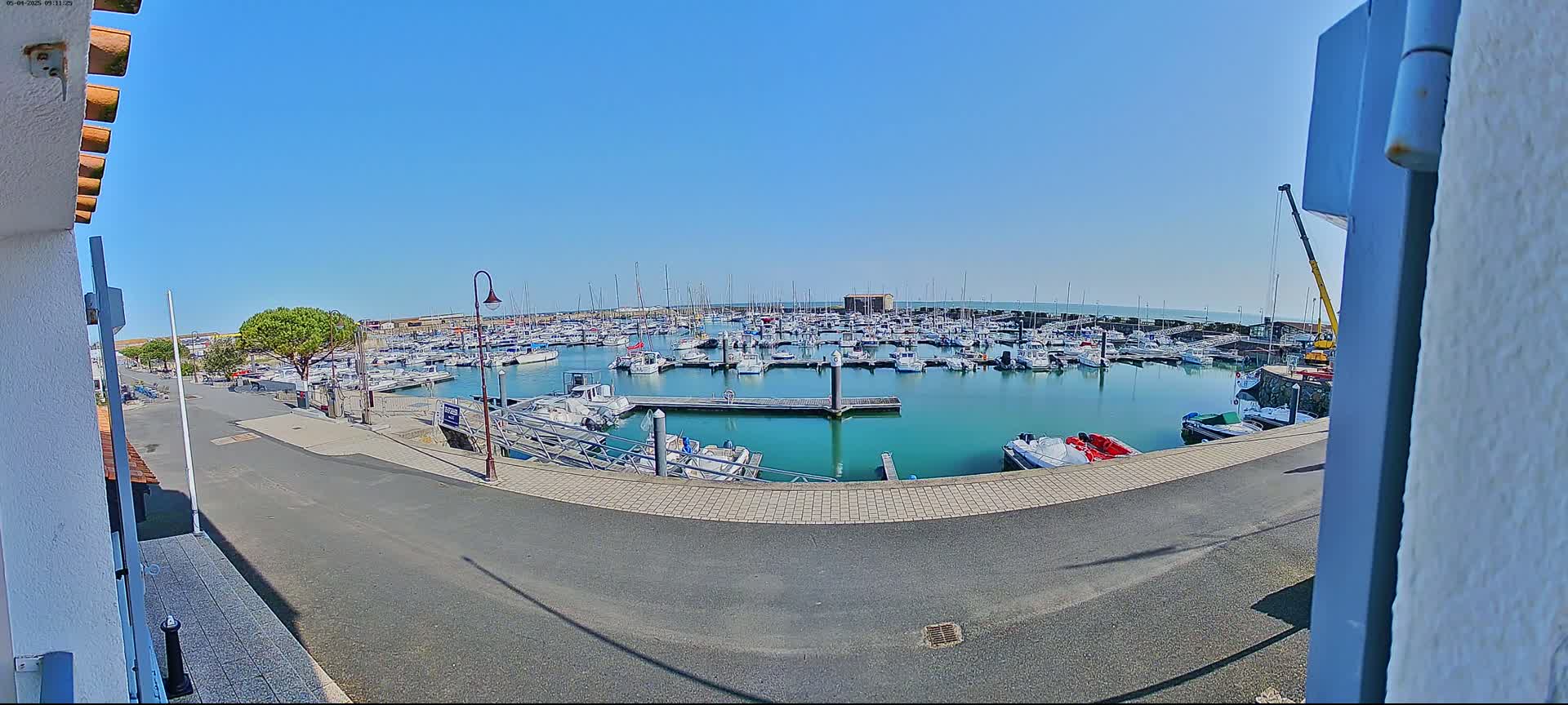 A marina filled with numerous boats is seen on a sunny day, viewed from a slightly elevated vantage point.