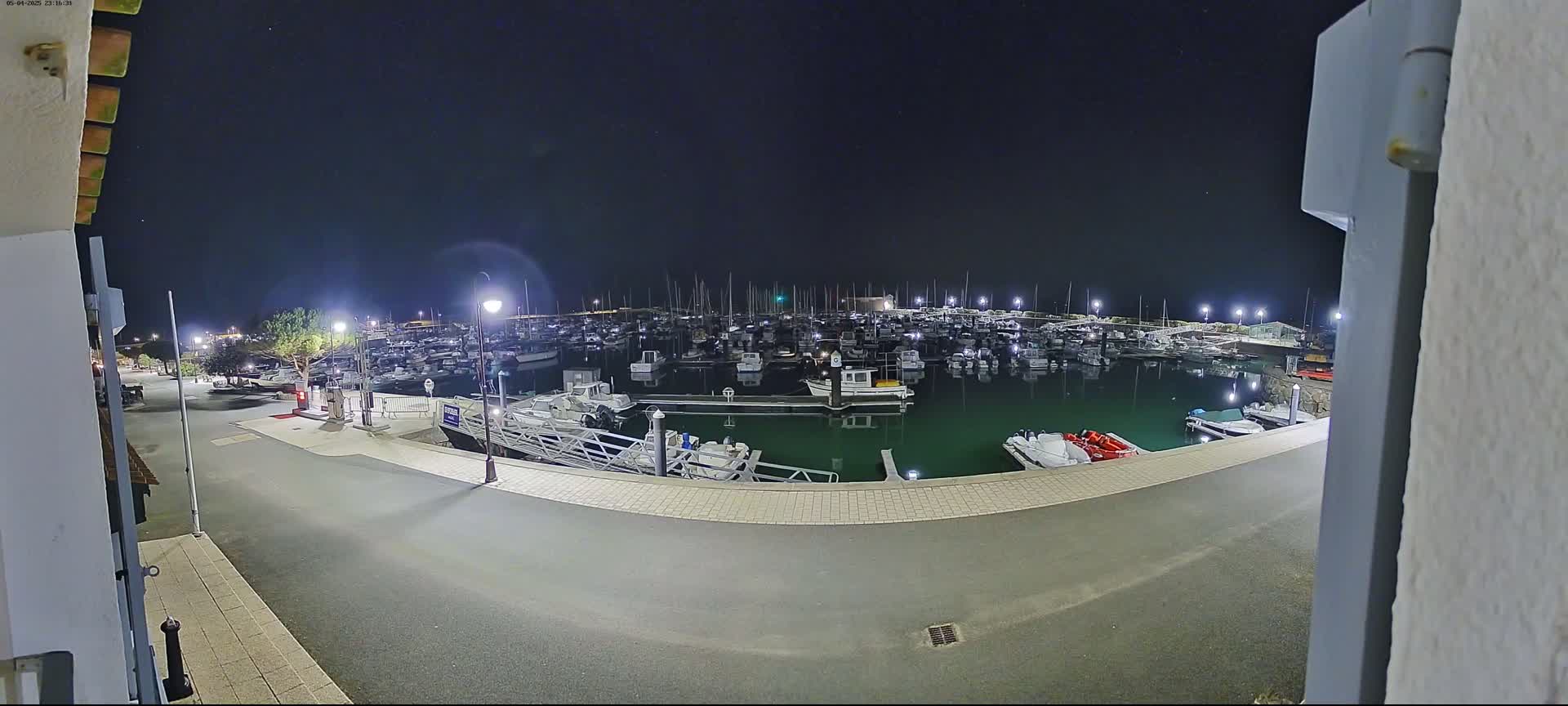A nighttime view of a marina filled with numerous boats, illuminated by artificial lights under a clear, starry sky.