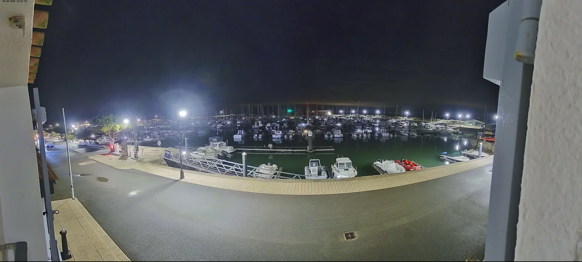 A nighttime view of a marina filled with numerous boats, illuminated by artificial lights under a clear, dark sky.