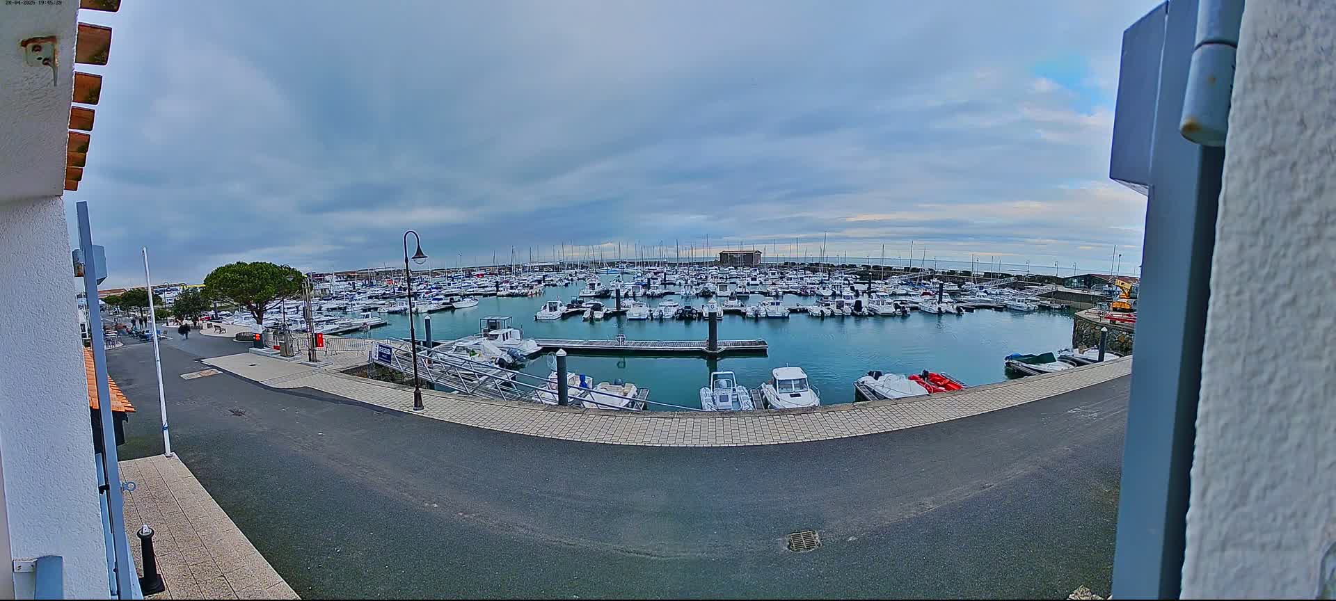 A harbor filled with numerous boats under a cloudy sky is viewed from a slightly elevated vantage point.