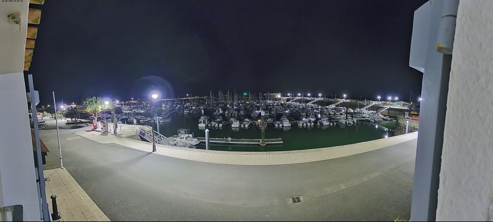 A nighttime view from a building shows a marina filled with numerous boats, illuminated by lights under a dark sky.