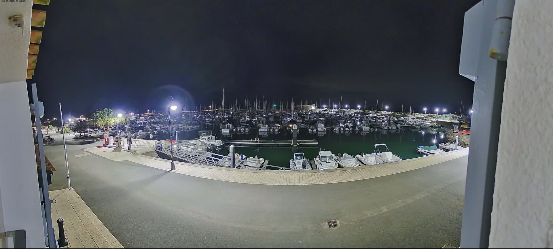 A nighttime view of a marina filled with numerous boats, illuminated by artificial lights under a dark sky.