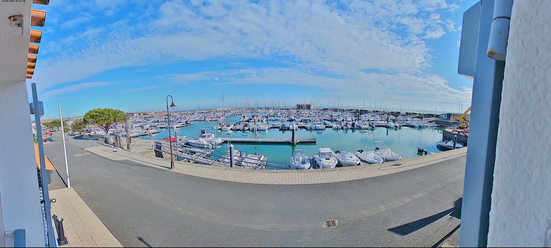A marina filled with numerous boats is seen on a sunny day with partly cloudy skies.