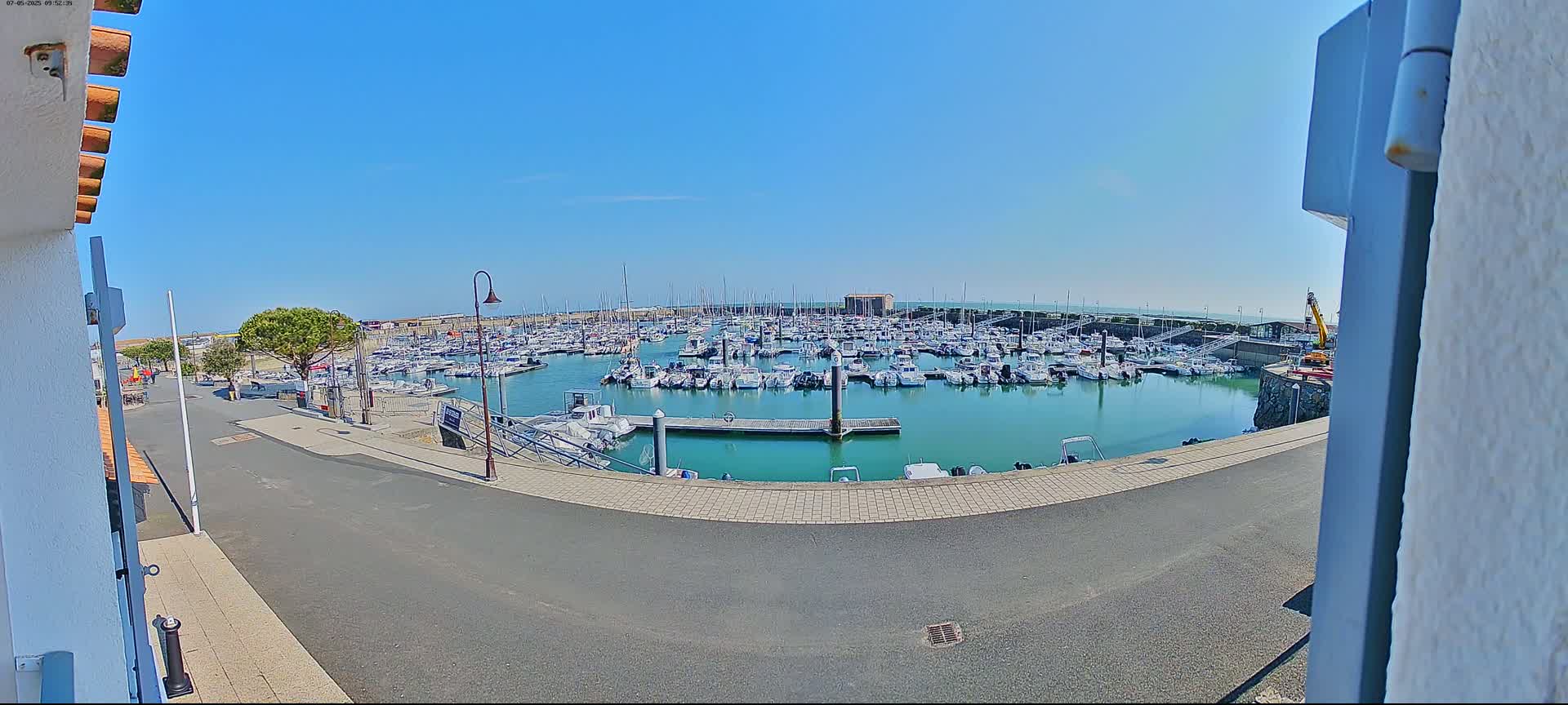 A marina filled with numerous boats is visible on a sunny day, viewed from a slightly elevated perspective.