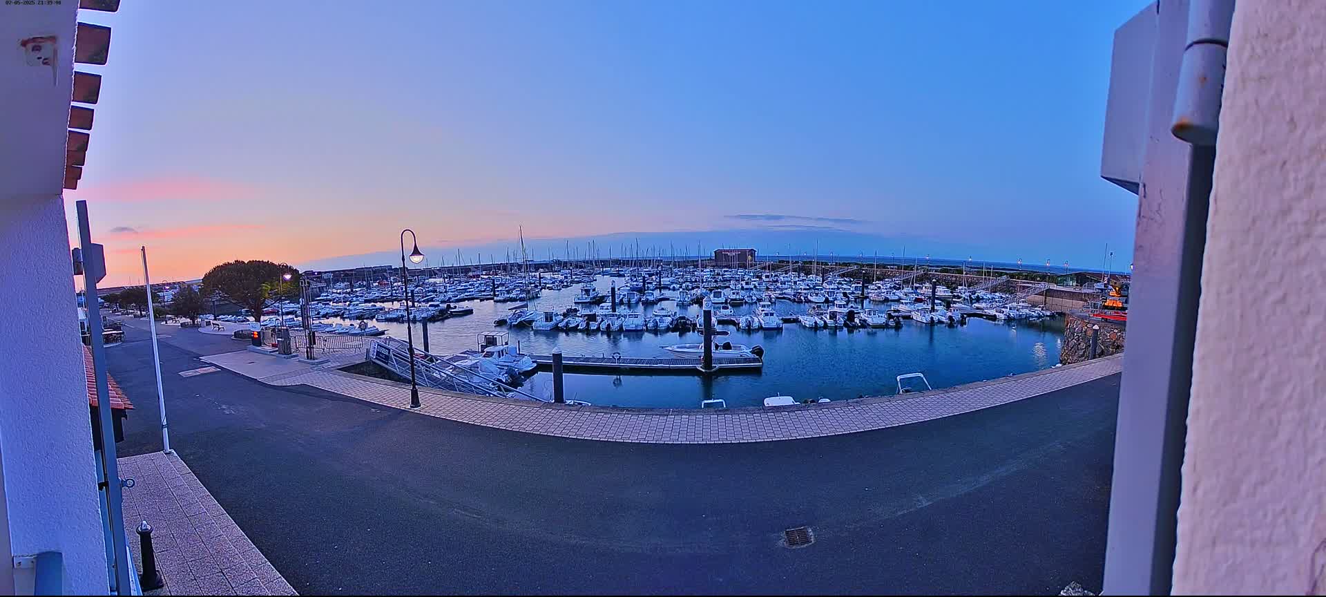 A marina filled with numerous boats is seen at dusk under a clear, twilight sky.