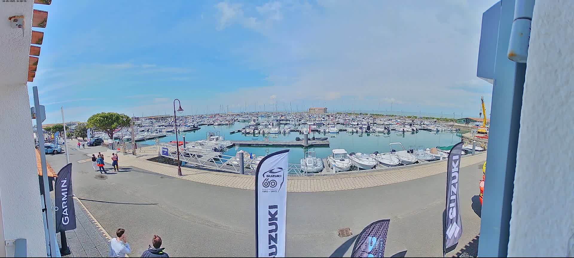 A marina filled with numerous boats under a mostly sunny sky is viewed from a slightly elevated vantage point.