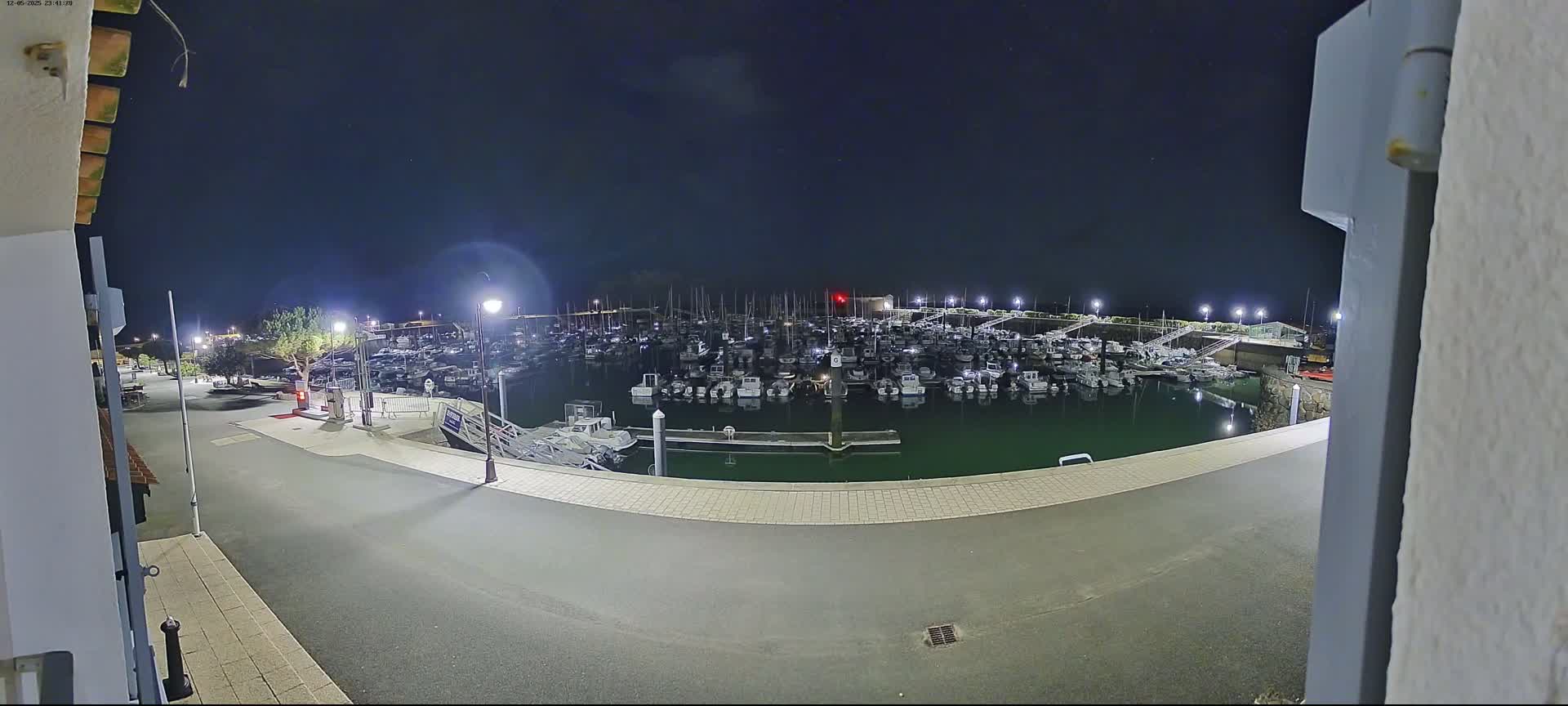 A marina filled with boats is visible at night under a clear, dark sky, viewed from a paved area nearby.