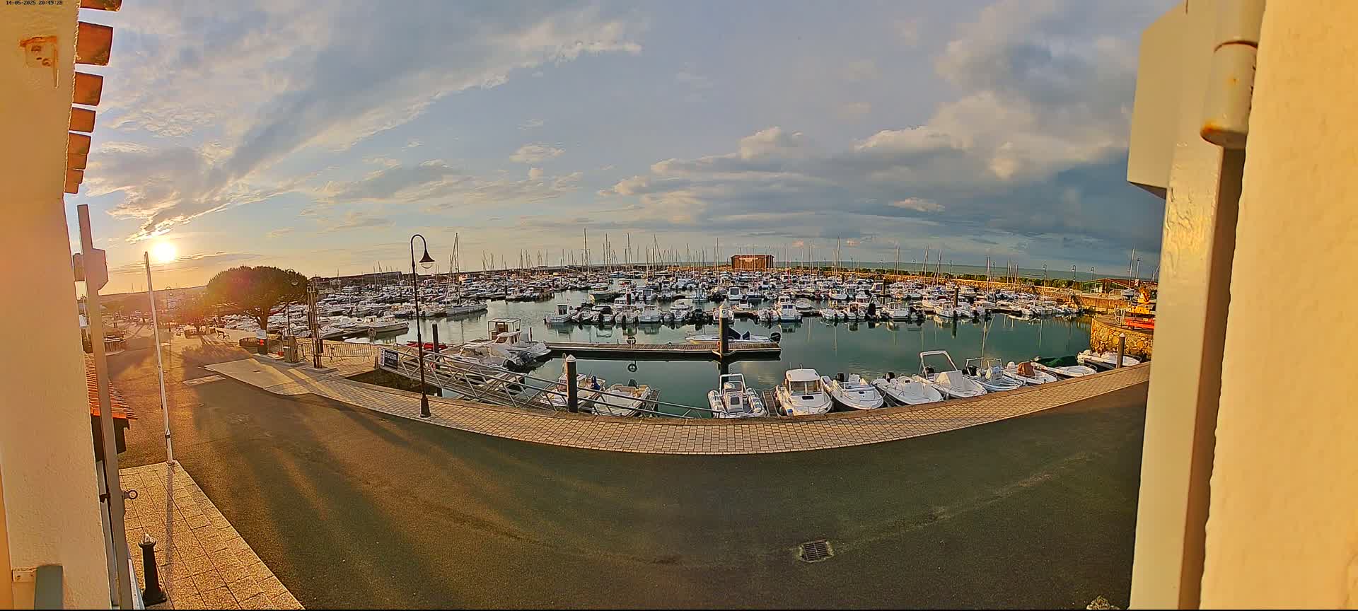 A marina filled with numerous boats is seen at sunset under a partly cloudy sky.
