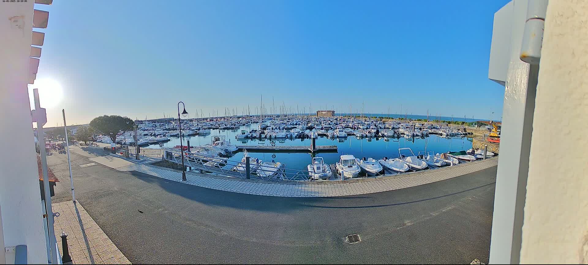 A sunny day reveals a marina filled with numerous boats of varying sizes, docked along a calm body of water.