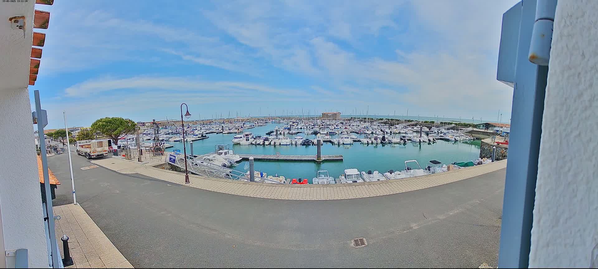 A marina filled with numerous boats under a partly cloudy sky is viewed from a slightly elevated position.