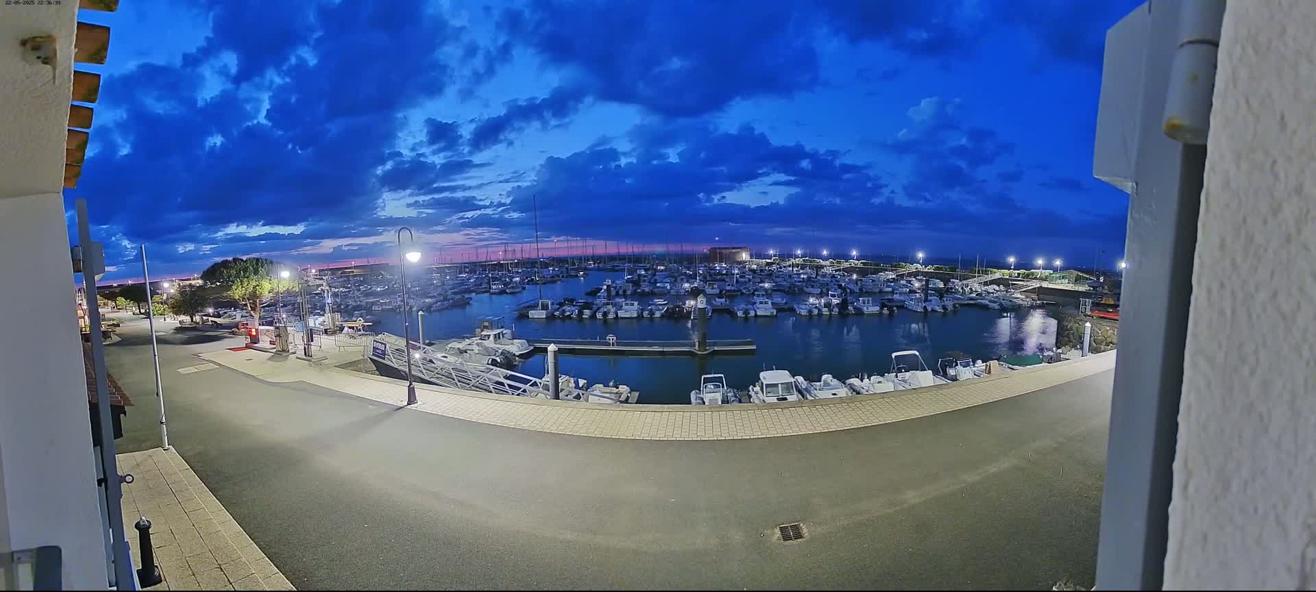 A marina filled with numerous boats is seen at twilight under a partly cloudy blue sky.
