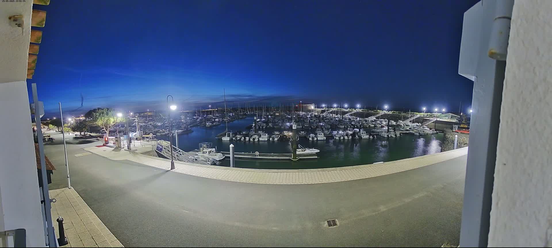 A marina filled with numerous boats is seen at night under a clear, dark blue sky.