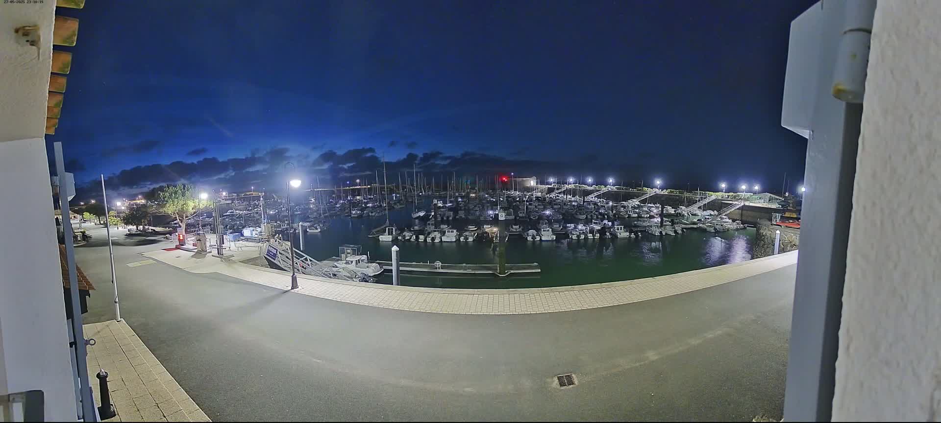 A nighttime view of a marina filled with boats under a dark blue, partly cloudy sky.