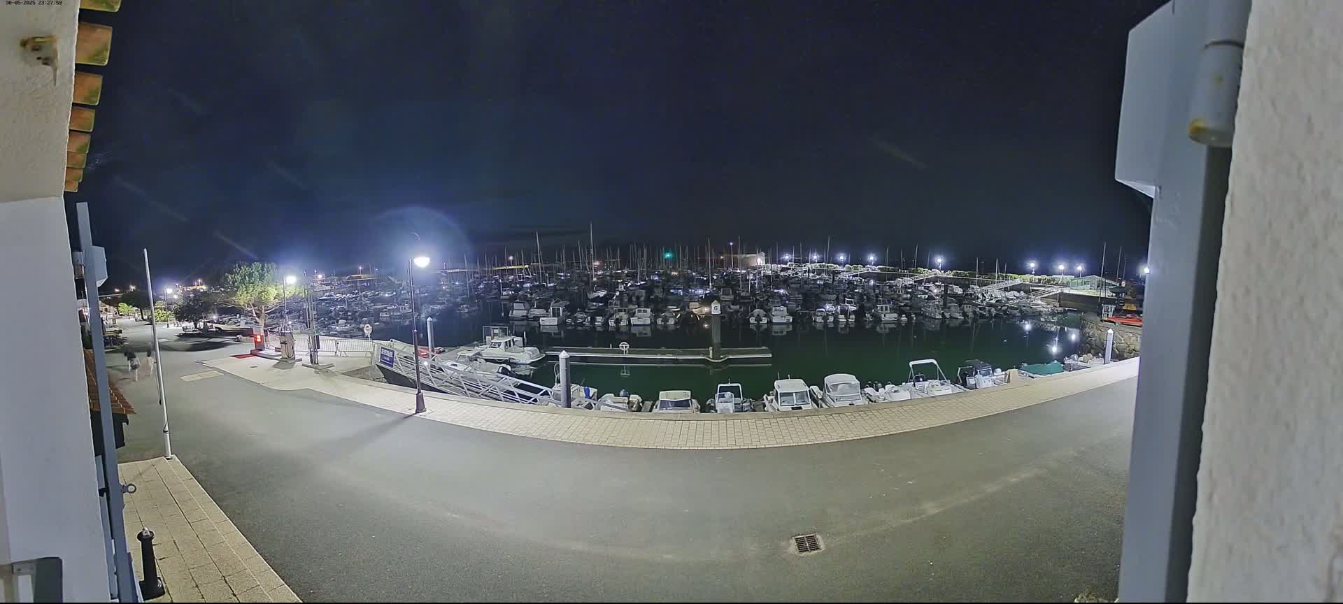 A nighttime view of a marina filled with many boats, illuminated by artificial lights under a dark sky.