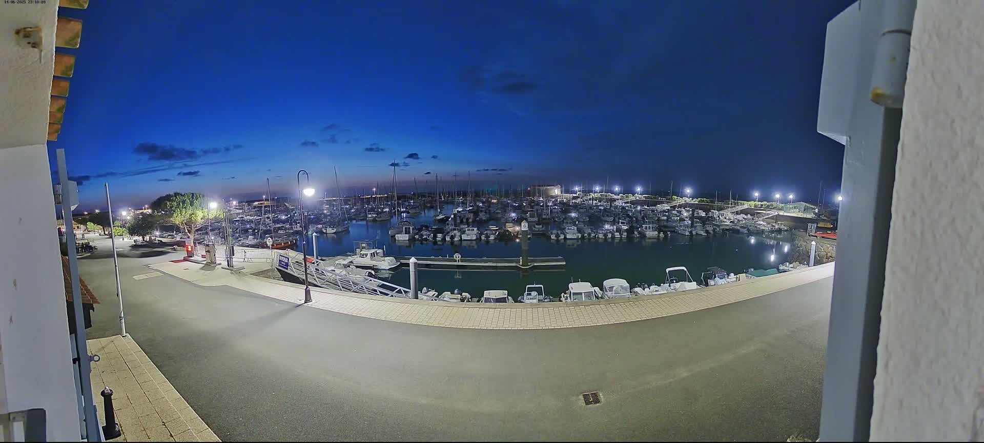 A marina filled with numerous boats under an overcast sky, with three people walking along the paved area next to the water.