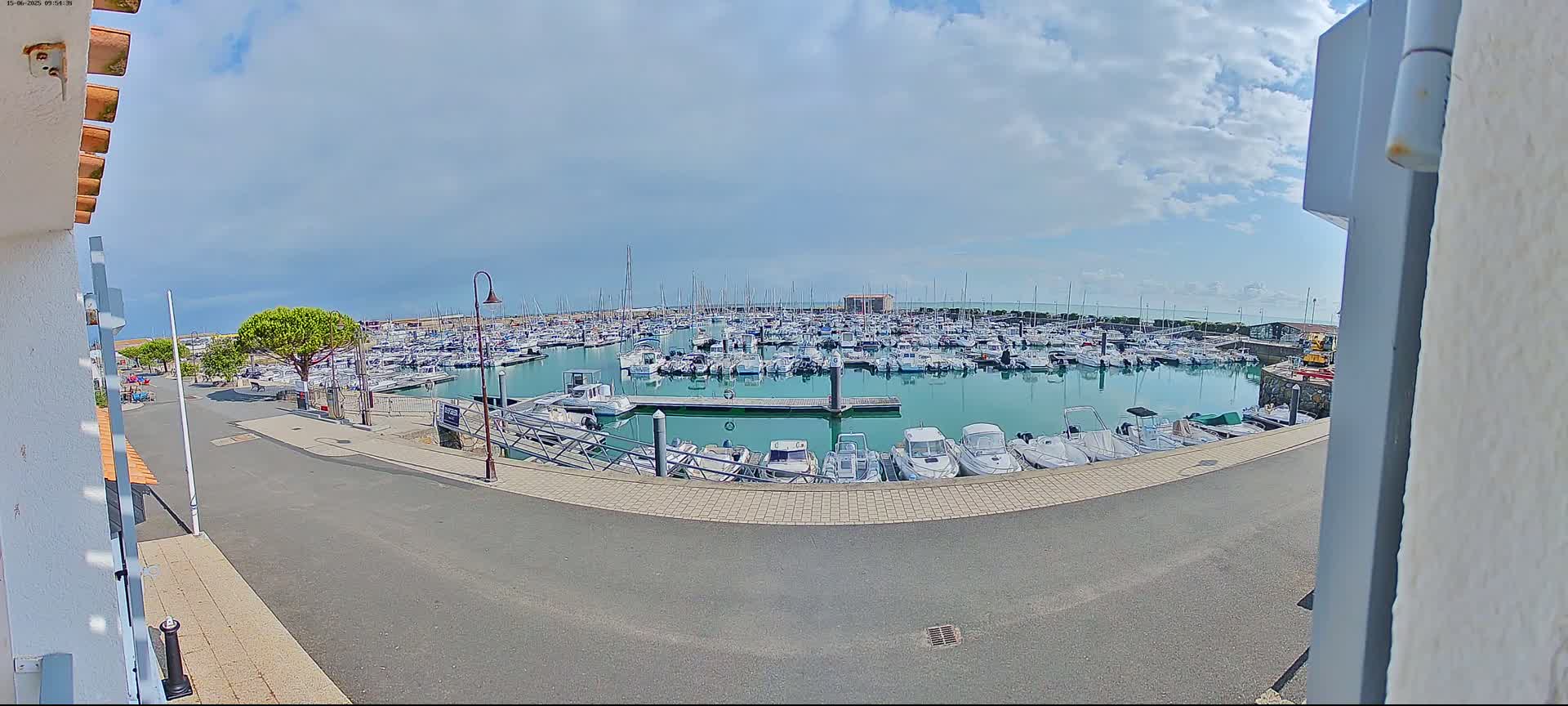 A marina filled with numerous boats under a partly cloudy sky is viewed from a slightly elevated position.