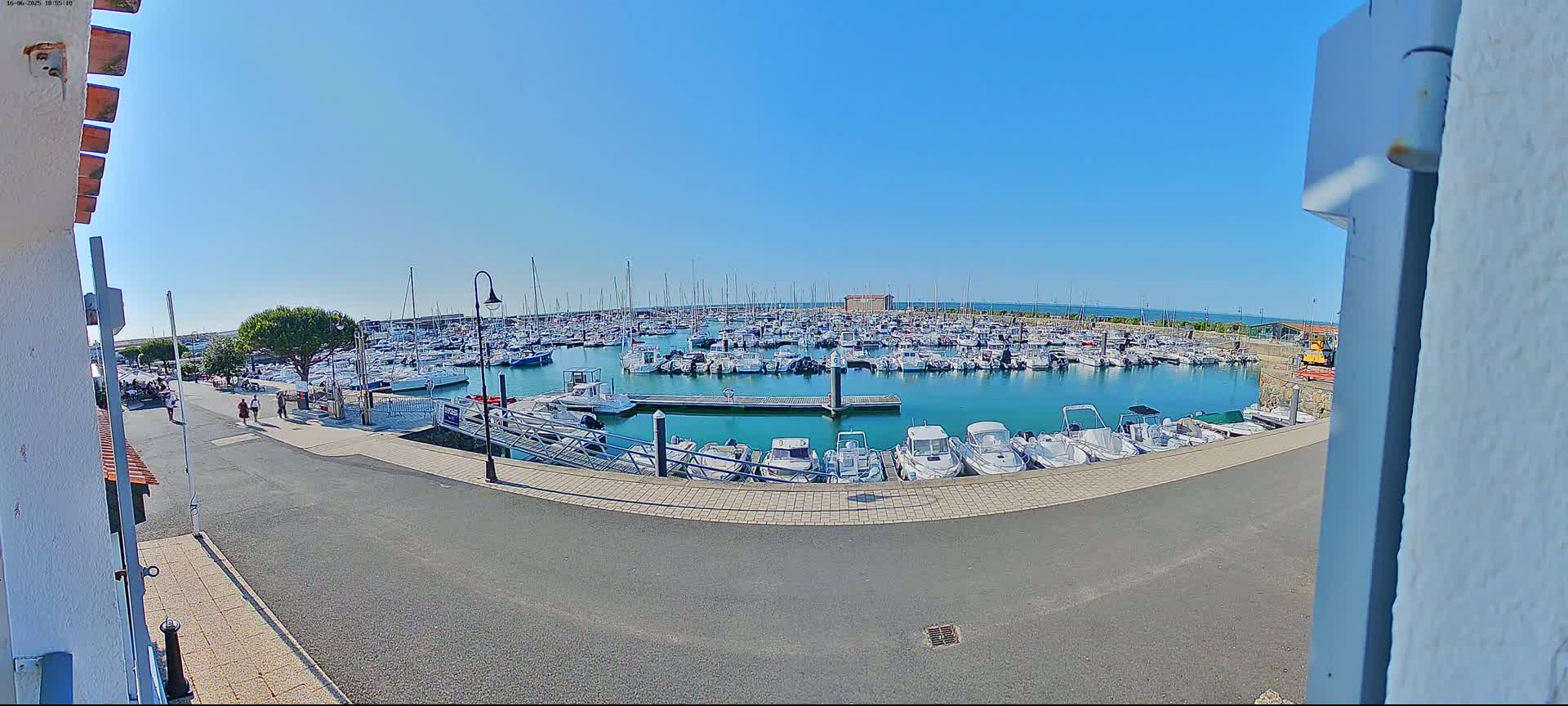 A marina filled with numerous boats on a sunny day is viewed from a slightly elevated position.