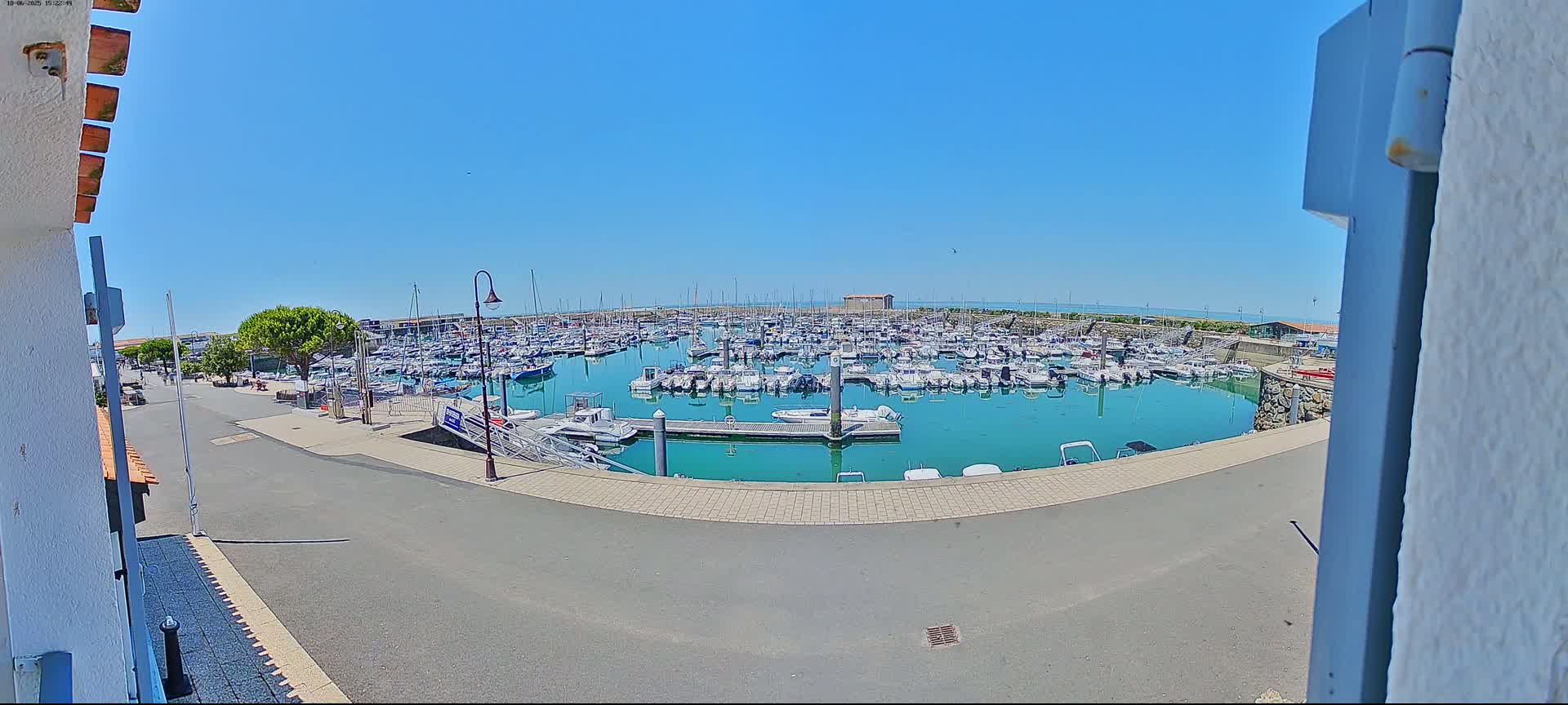 A marina filled with numerous boats is seen on a sunny day, viewed from a slightly elevated position.