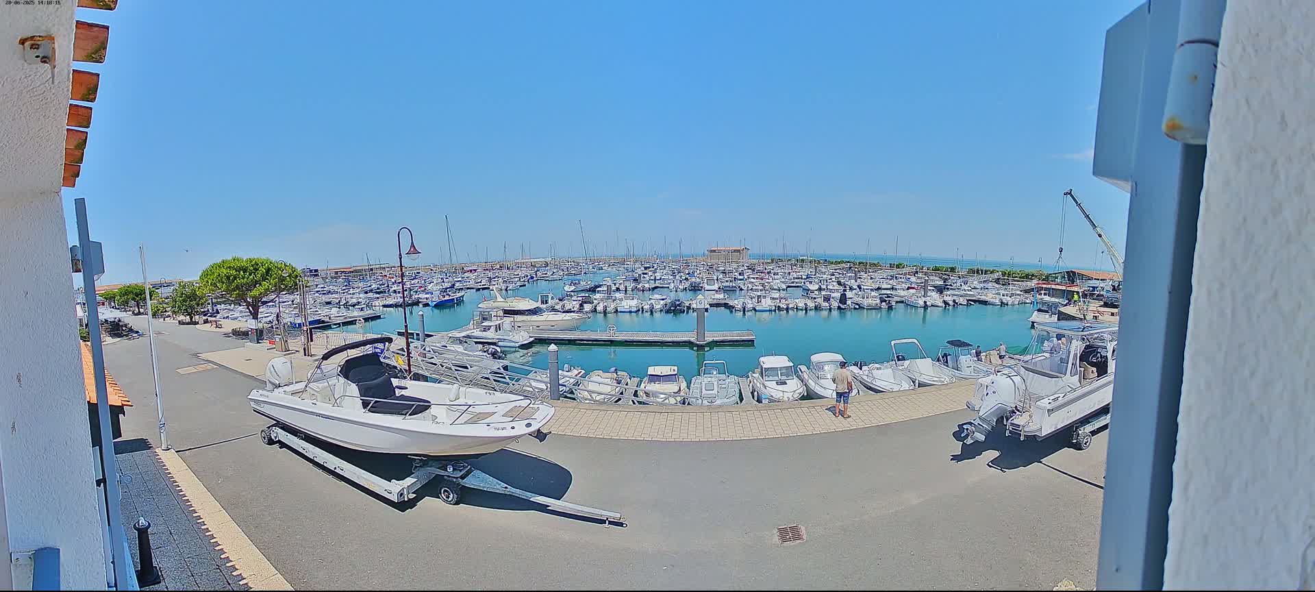 A marina filled with numerous boats on a sunny day, with a few boats on trailers near the edge of the paved area.