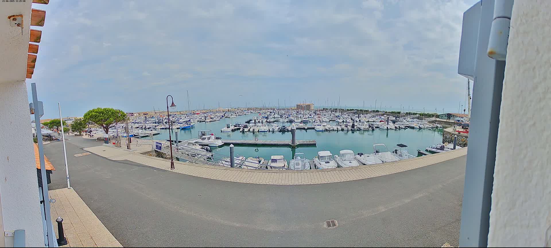 A marina filled with numerous boats is visible under a partly cloudy sky.