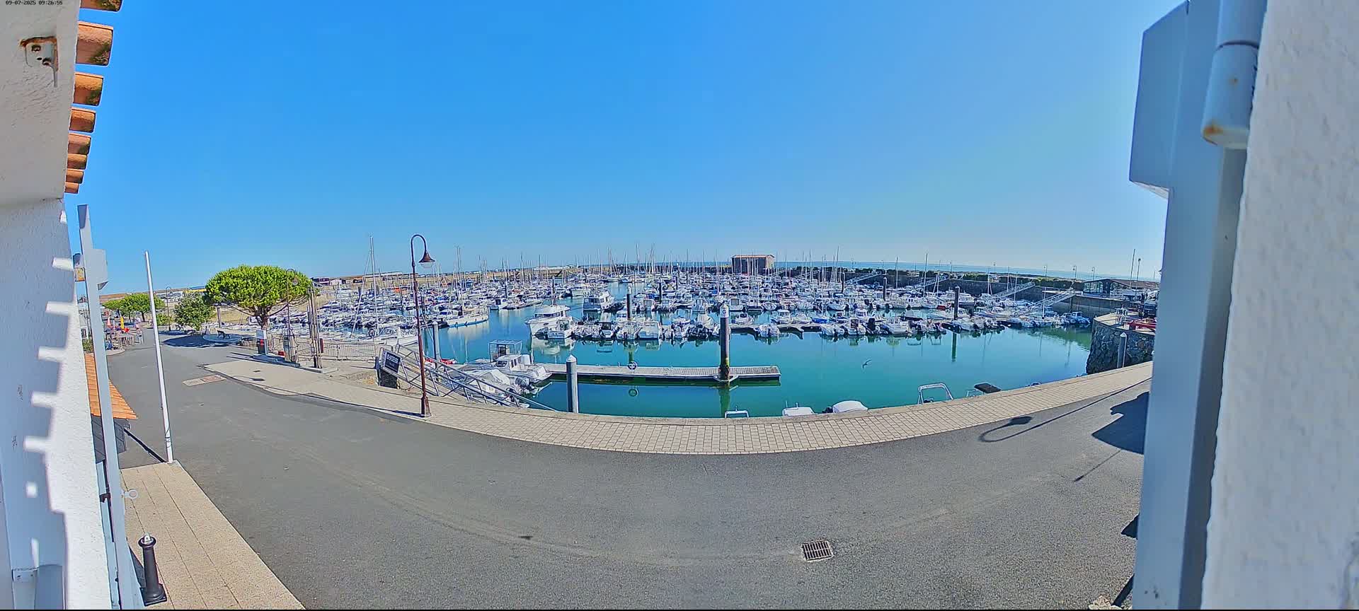 A marina filled with numerous boats sits under a clear blue sky on a sunny day.