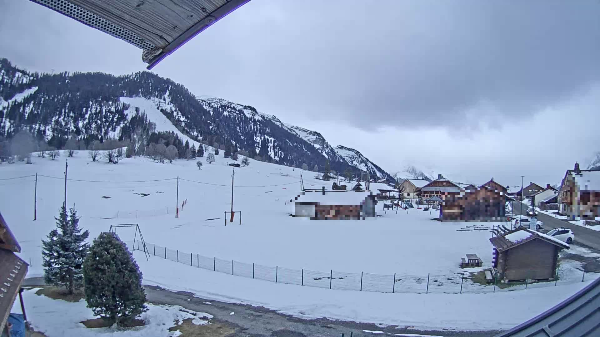 A snow-covered village nestled in a valley between snow-capped mountains under an overcast sky.