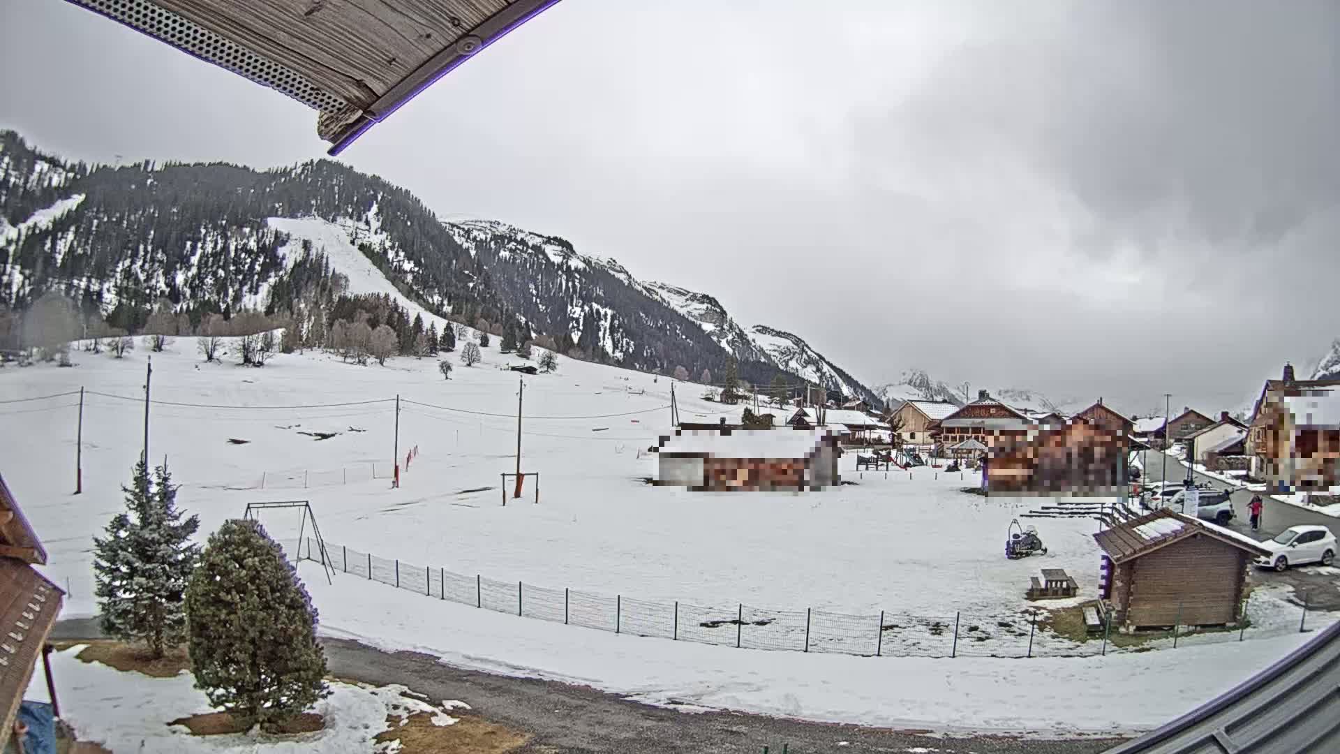 A snow-covered village nestled in a valley between mountains under an overcast sky.
