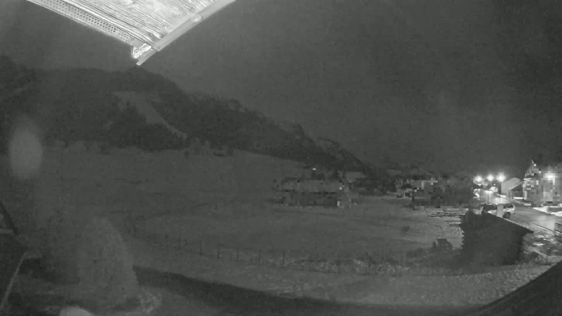 A nighttime, snow-covered landscape is seen from a high vantage point, showing a small village nestled below a hill.