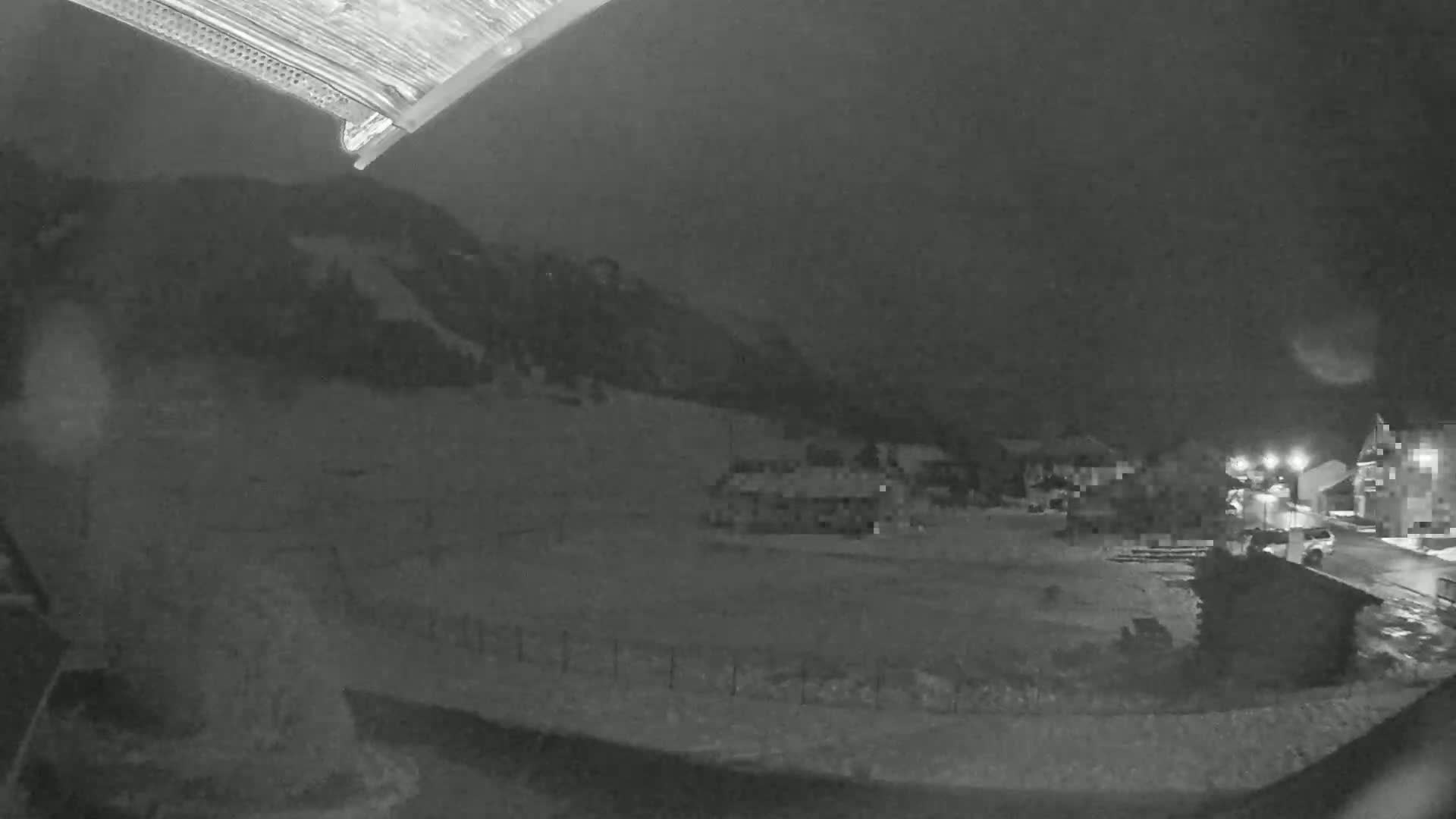 A nighttime, snowy scene shows a village nestled below a dark mountain under a cloudy sky.