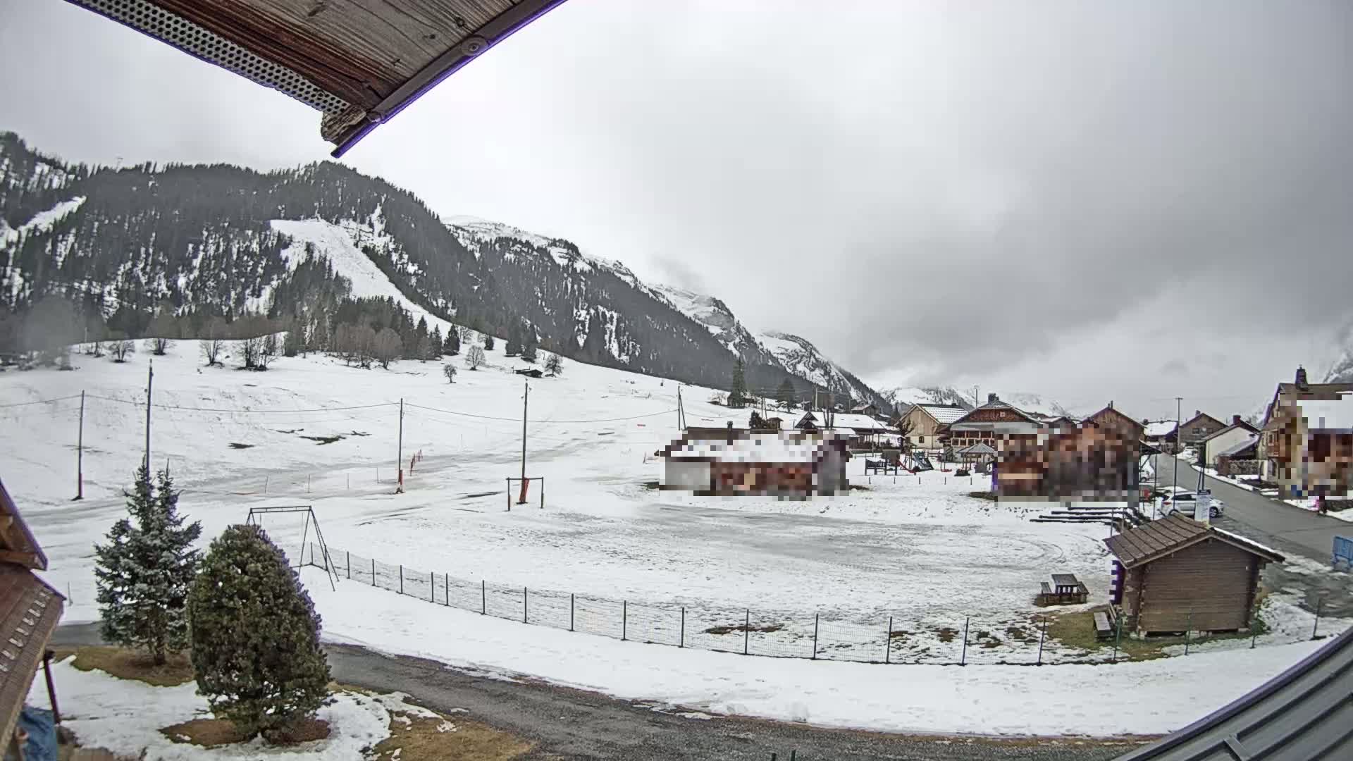A snow-covered village nestled in a valley between mountains under an overcast sky.