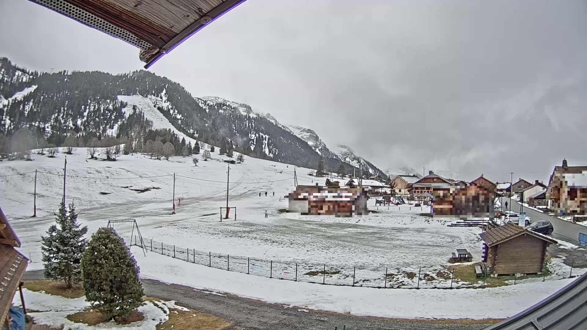 A snow-covered village nestled in a valley between mountains under an overcast sky.